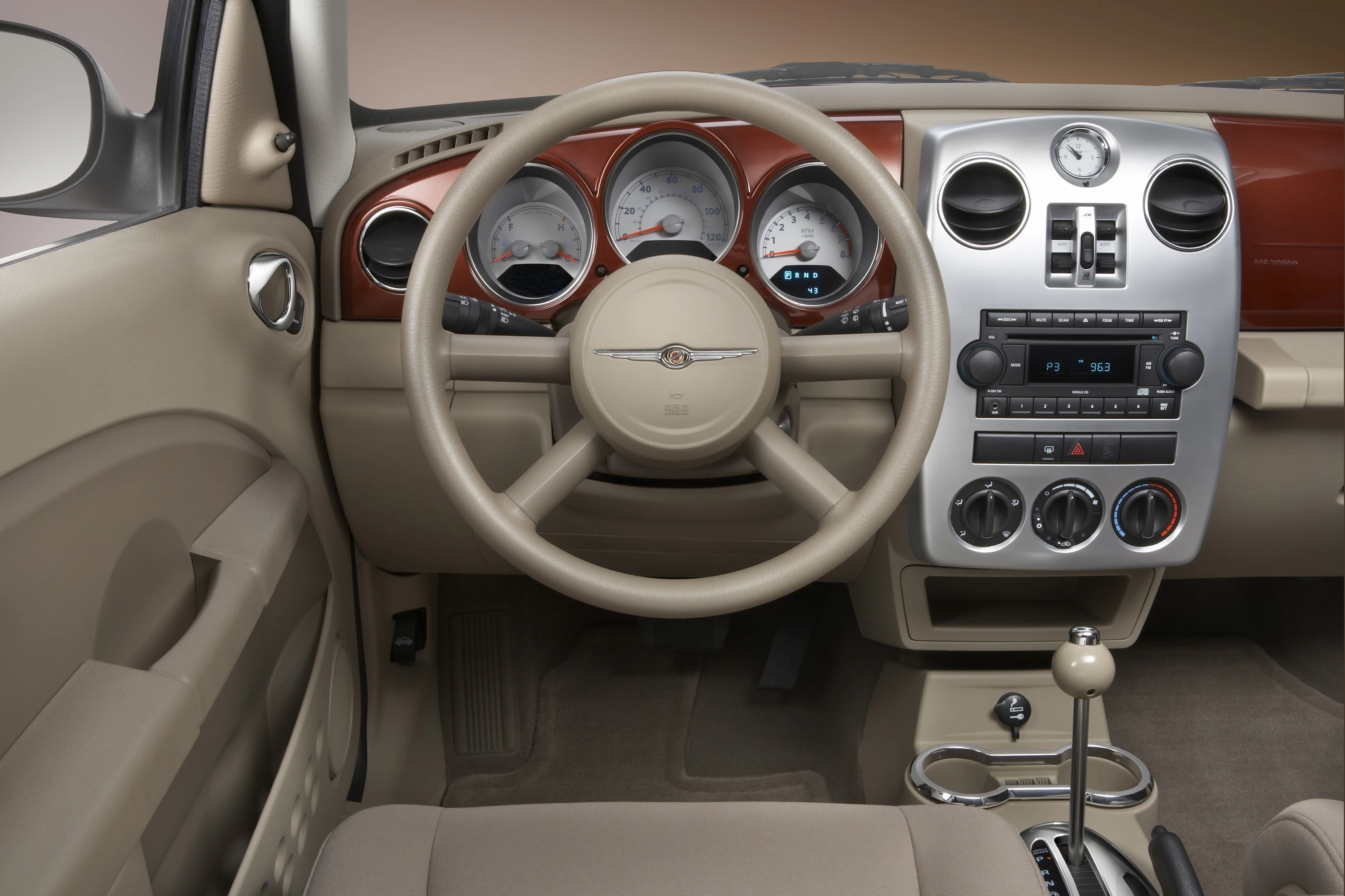 Innenraum eines Autos mit beigem Interieur. Sicht auf das Lenkrad, Armaturenbrett mit Rundanzeigen, Mittelkonsolen und Schalthebel.