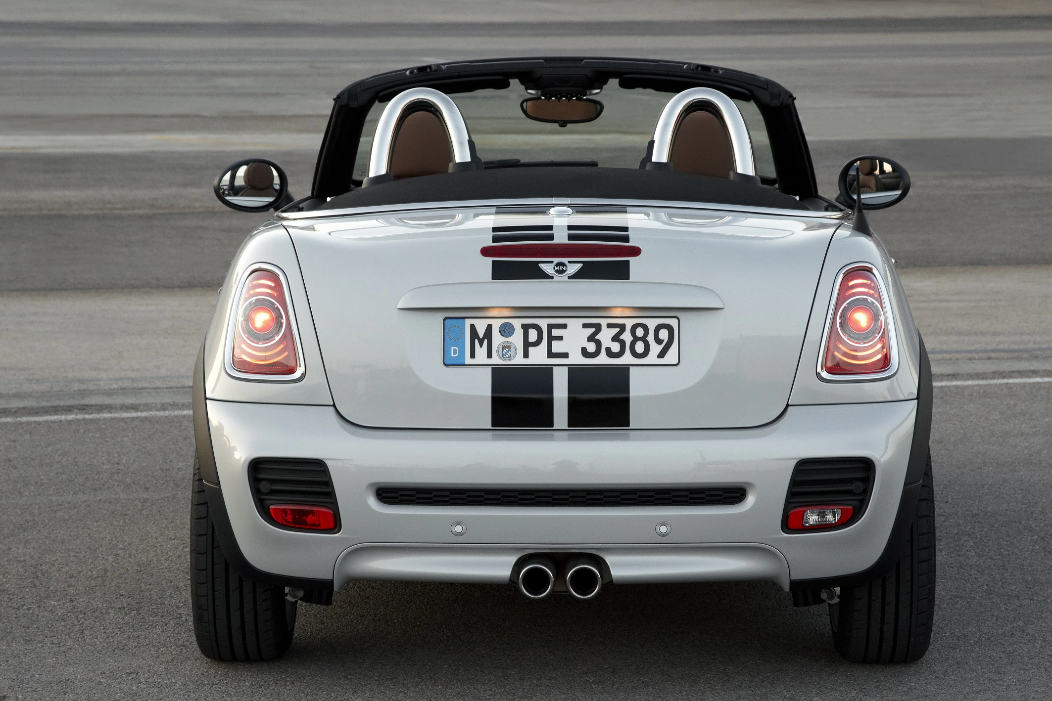 Silberner Cabrio mit schwarzen Streifen, Heckansicht. Sichtbares Nummernschild: MÖPE 3389. Fahrzeug auf einer grauen Oberfläche geparkt.