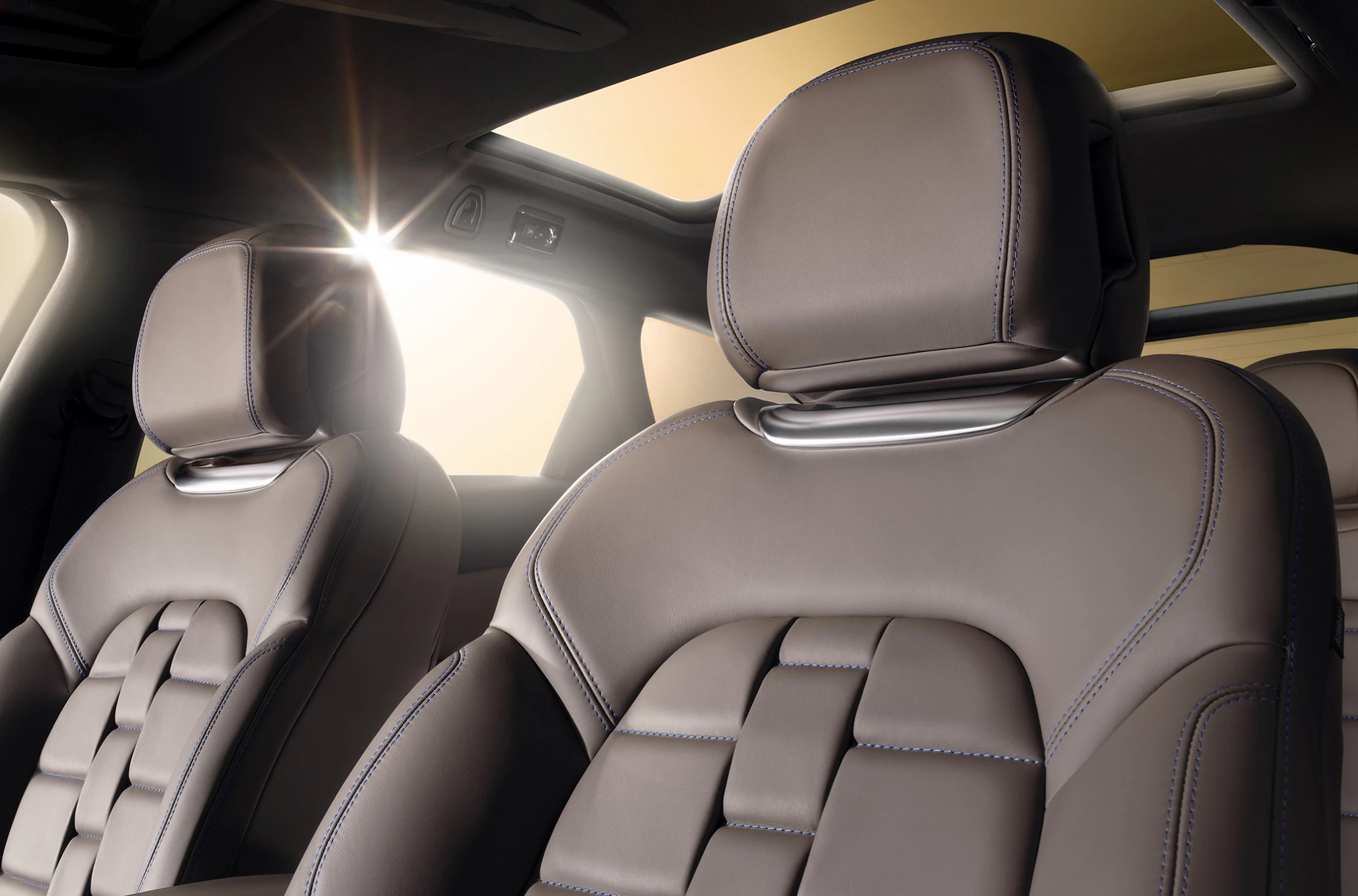 Vordersitze eines Autos mit braunem Leder, modernem Design und einem offenen Schiebedach, durch das Sonnenlicht hereinfällt.