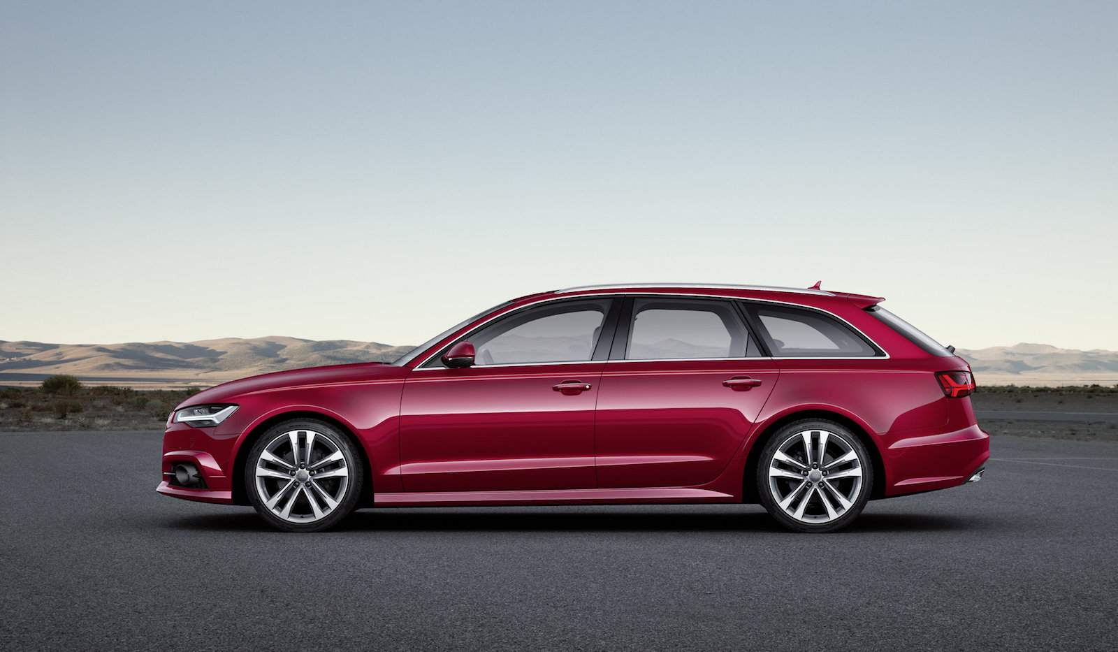 Roter Kombiwagen parkt auf leerem Platz, seitliche Ansicht. Hintergrund mit blauem Himmel und fernen Hügeln.