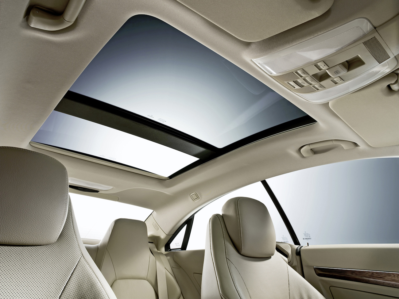 Innenraum eines Autos mit beigen Ledersitzen und Panoramadach. Das Dach ist teils geöffnet und hell beleuchtet.