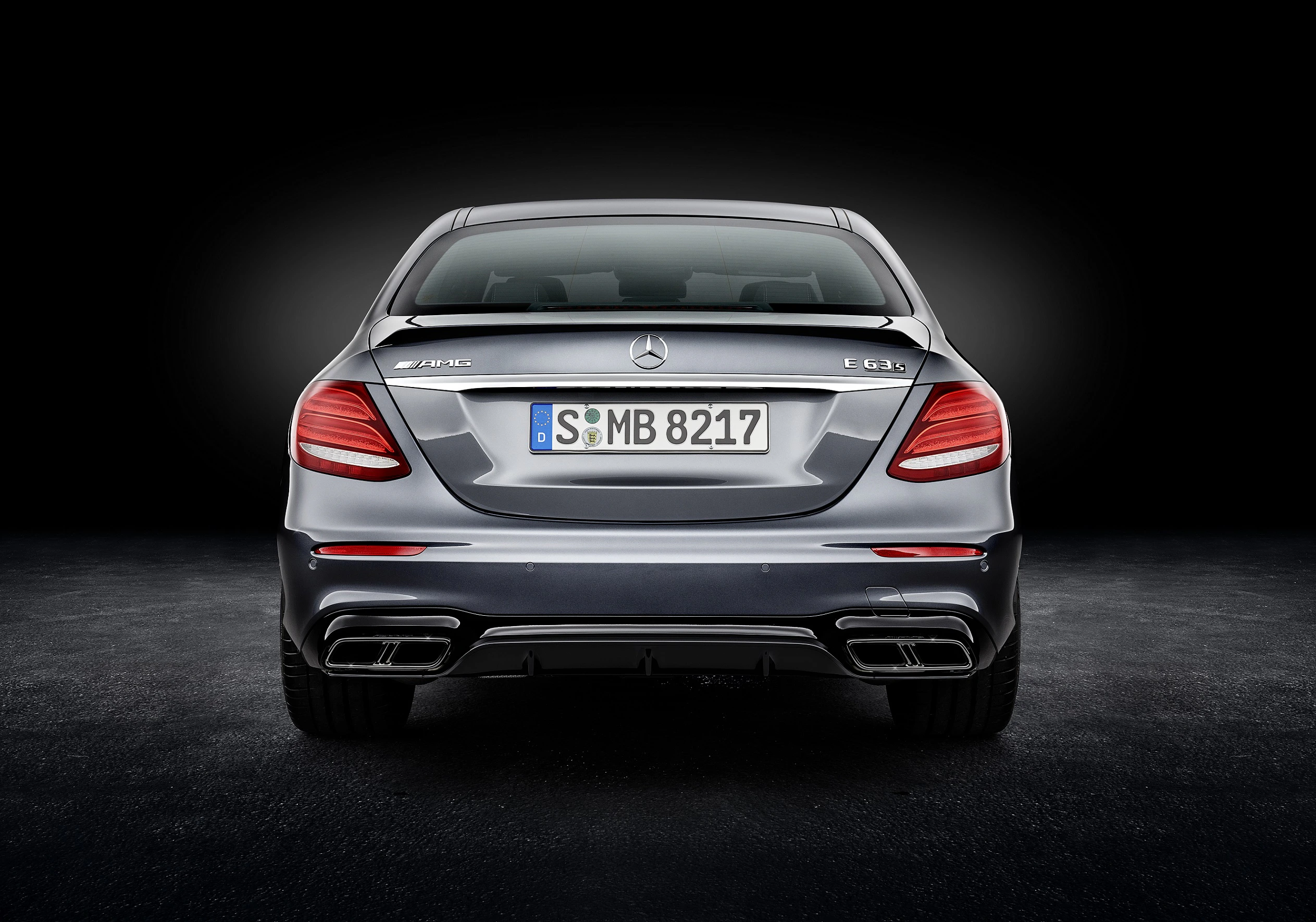 Rückansicht eines silbernen Mercedes-AMG E 63 S mit beleuchtetem Hintergrund, sportliches Design mit markanten Auspuffanlagen und Nummernschild.