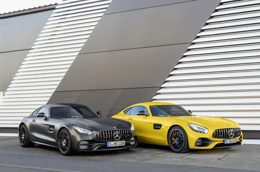 Zwei sportliche Mercedes-AMG GT Coupés, ein schwarzes und ein gelbes, parken vor einer modernen, gestreiften Gebäudefassade.