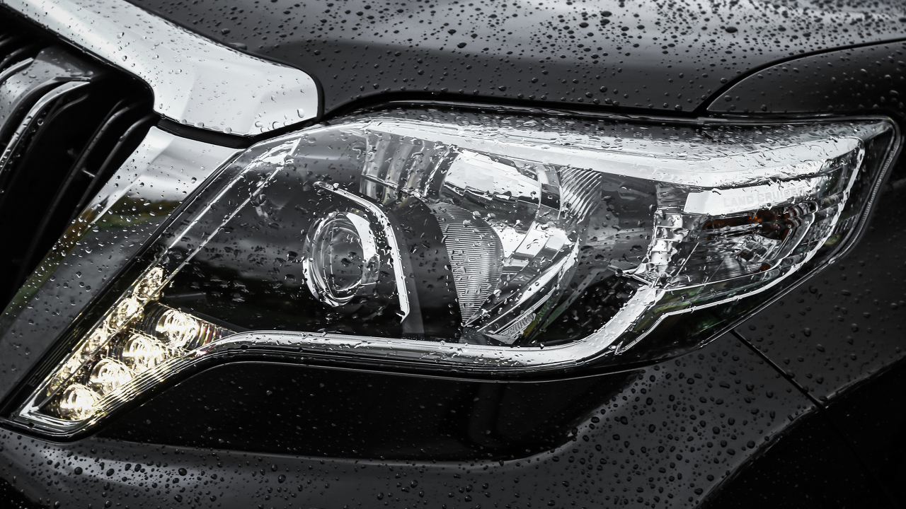 Nahaufnahme eines nassen Autoscheinwerfers mit Wassertropfen auf der Oberfläche. Klar strukturiertes und modernes Design.