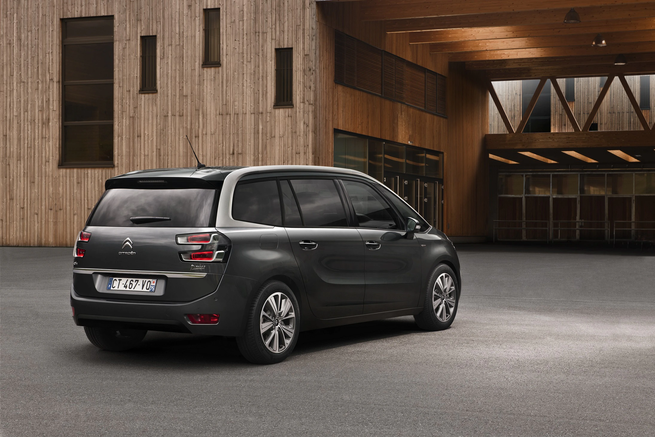 Ein grauer Citroën Grand C4 Picasso parkt vor einem modernen Gebäude aus Holz mit großen Fenstern.