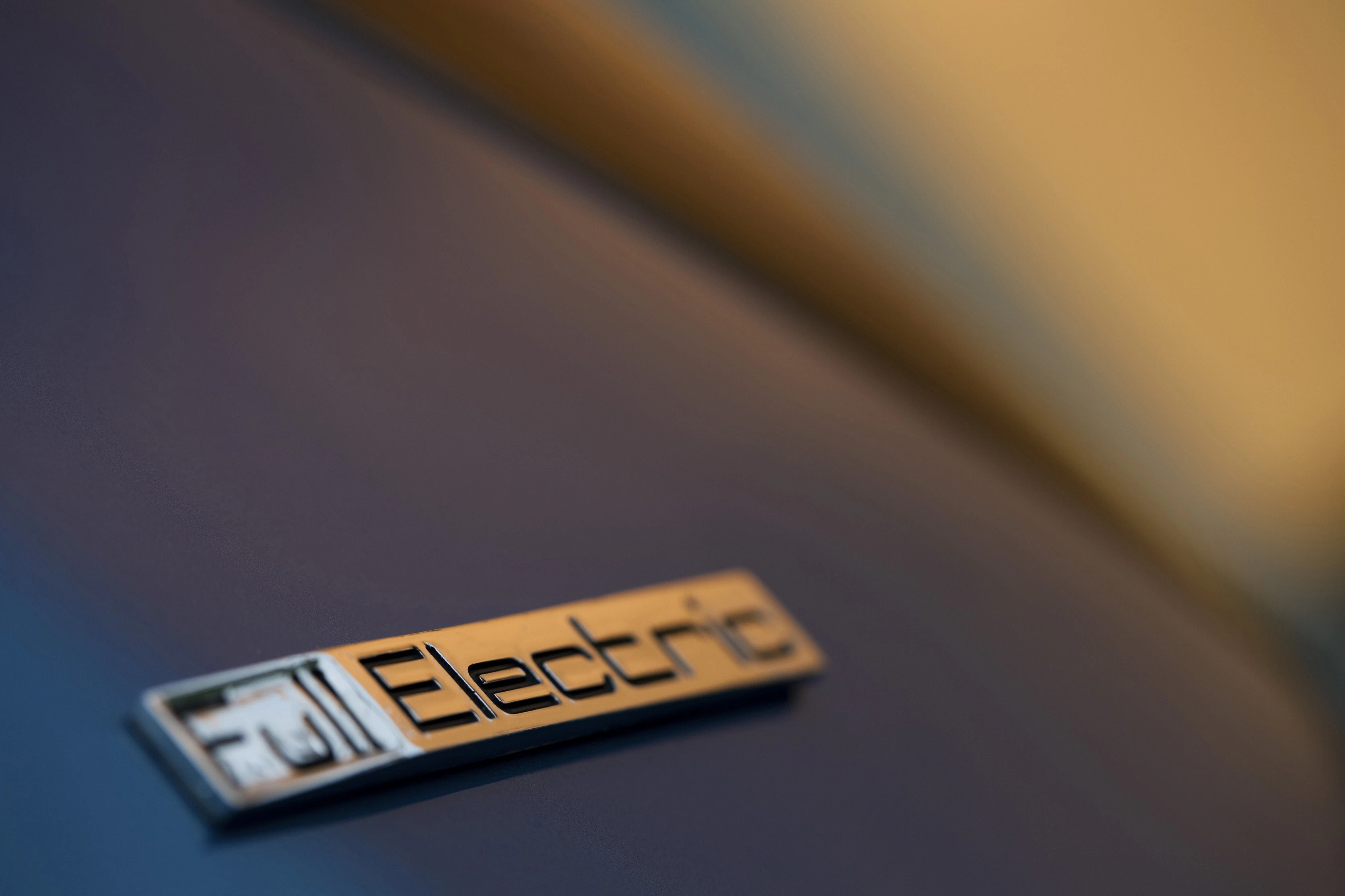 Nahaufnahme eines Emblems mit der Aufschrift "Electric" auf einem Fahrzeug in Unschärfe.