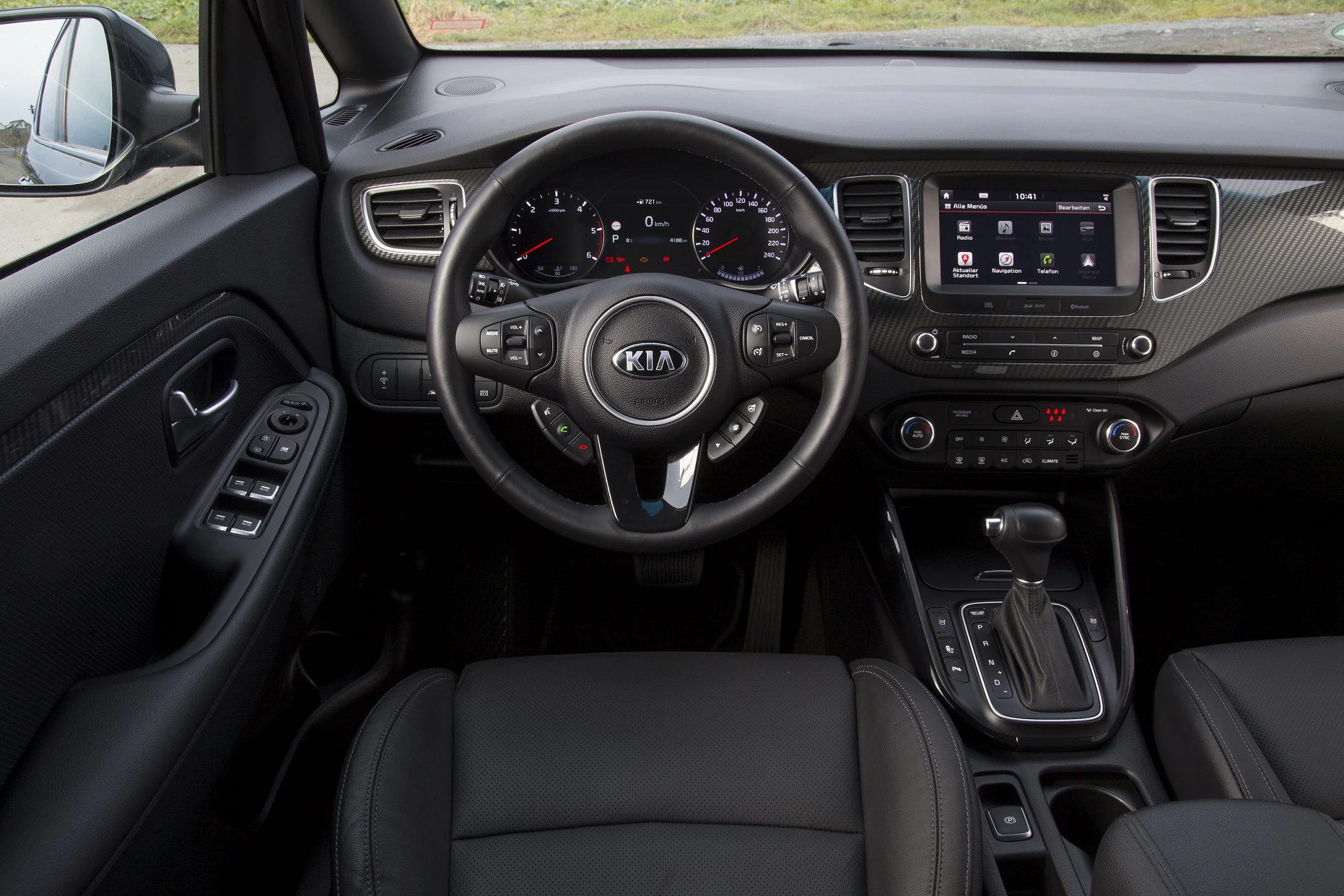 Innenraum eines modernen Autos mit dem Kia-Logo auf dem Lenkrad, Tachometer, Touchscreen-Display und Automatikschaltung.
