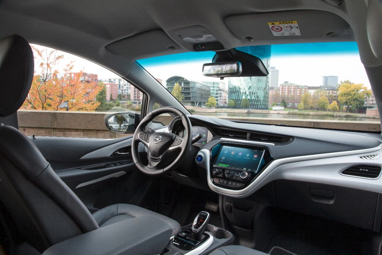 Innenraum eines modernen Autos mit Sicht auf die Stadt im Hintergrund durch die Windschutzscheibe. Lenkrad links, Touchscreen in der Mitte.