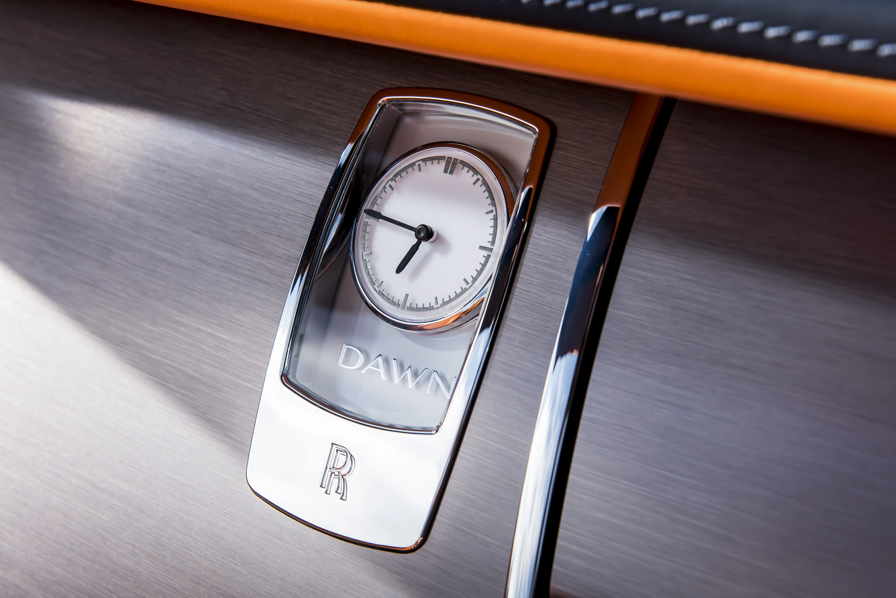 Uhr in einem Luxusauto-Armaturenbrett, glänzend und edel mit der Aufschrift "DAWN" und dem Logo von Rolls-Royce darunter.