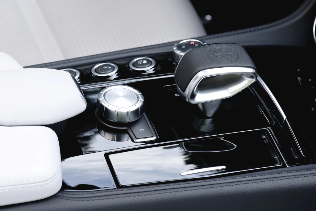 Nahaufnahme einer luxuriösen Auto-Mittelkonsole mit schwarzer Schaltung, silbernem Drehknopf und weißen Armlehnen.