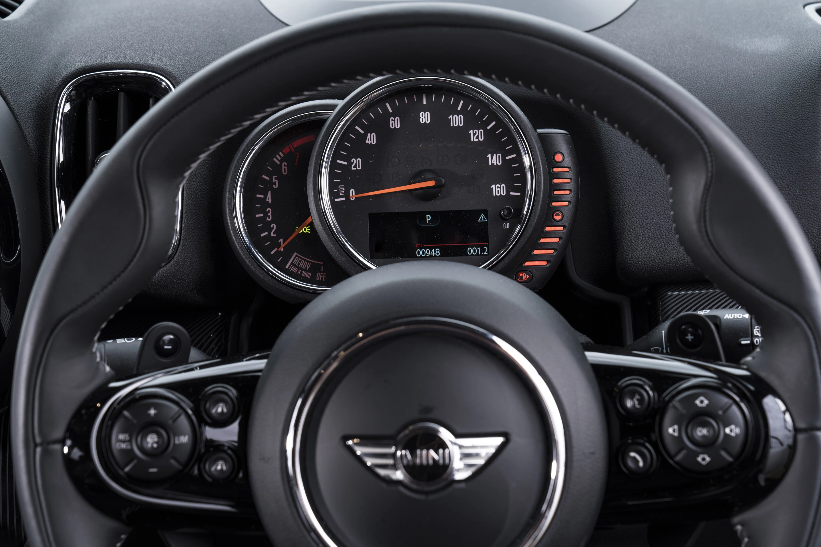 Lenkrad und Armaturenbrett eines MINIs, Tachometer in der Mitte, zeigt knapp 0 km/h. Bedienelemente am Lenkrad sichtbar.