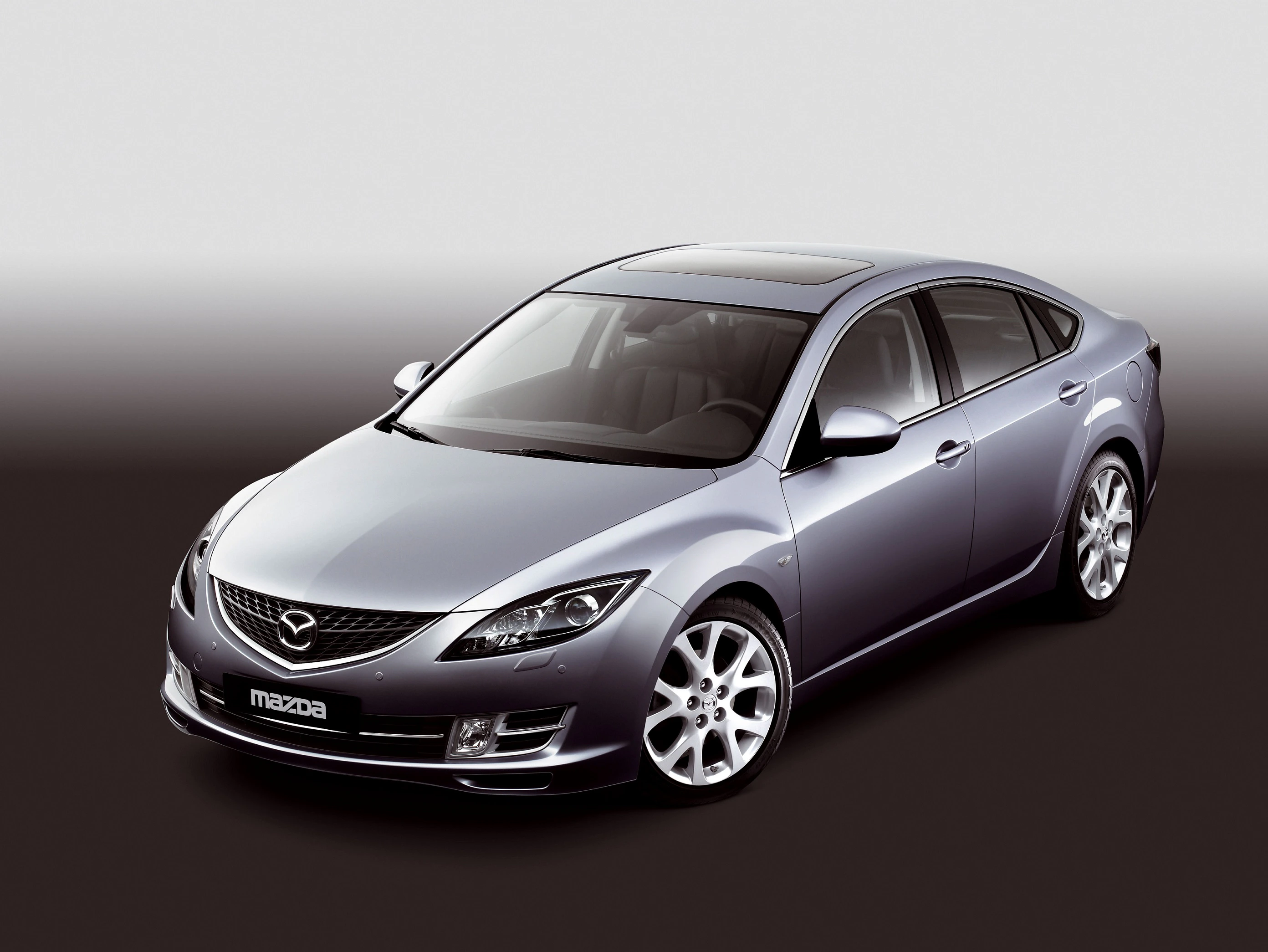 Silberner Mazda 6 mit elegantem Design, schrägem Heck, glänzenden Felgen und klaren Linien, vor grauem Hintergrund.