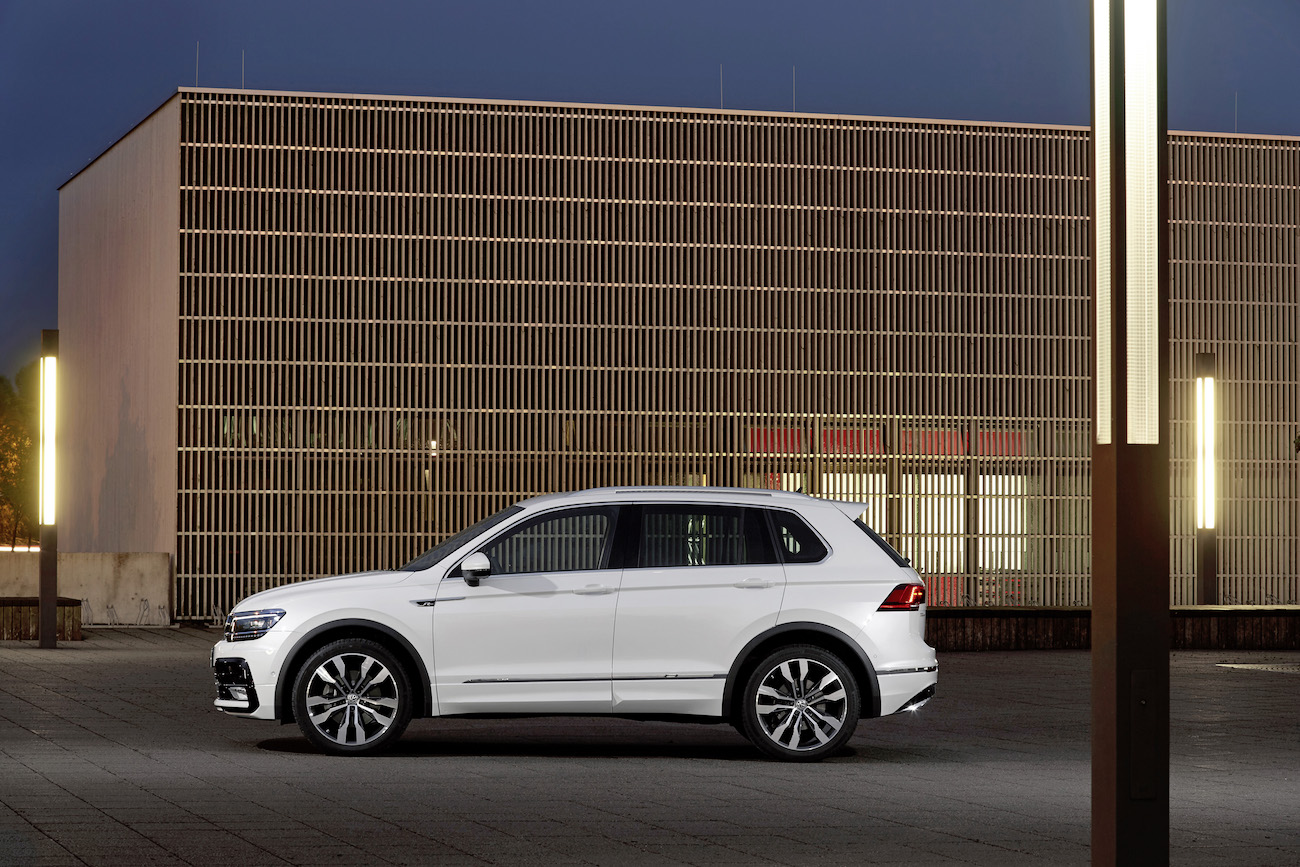 Weißer SUV, seitliche Ansicht, steht vor einem modernen Gebäude in der Dämmerung, beleuchtet von mehreren modernen Straßenlaternen.