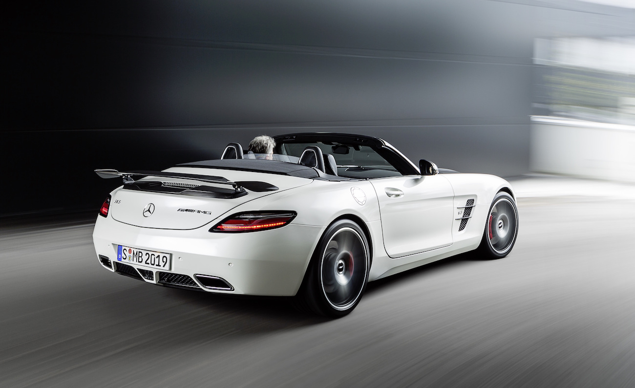 Weißer Sportwagen mit offenem Verdeck fährt dynamisch auf einer Straße. Moderne Linien und schnelle Bewegung sind erkennbar.