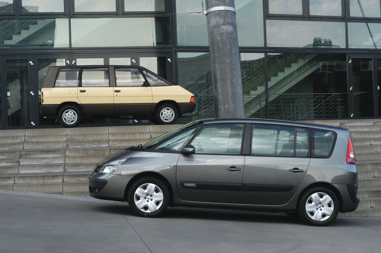 Zwei Autos vor einem modernen Gebäude: Ein beiges Auto steht oben auf Treppe, ein graues Auto steht unten davor seitlich.
