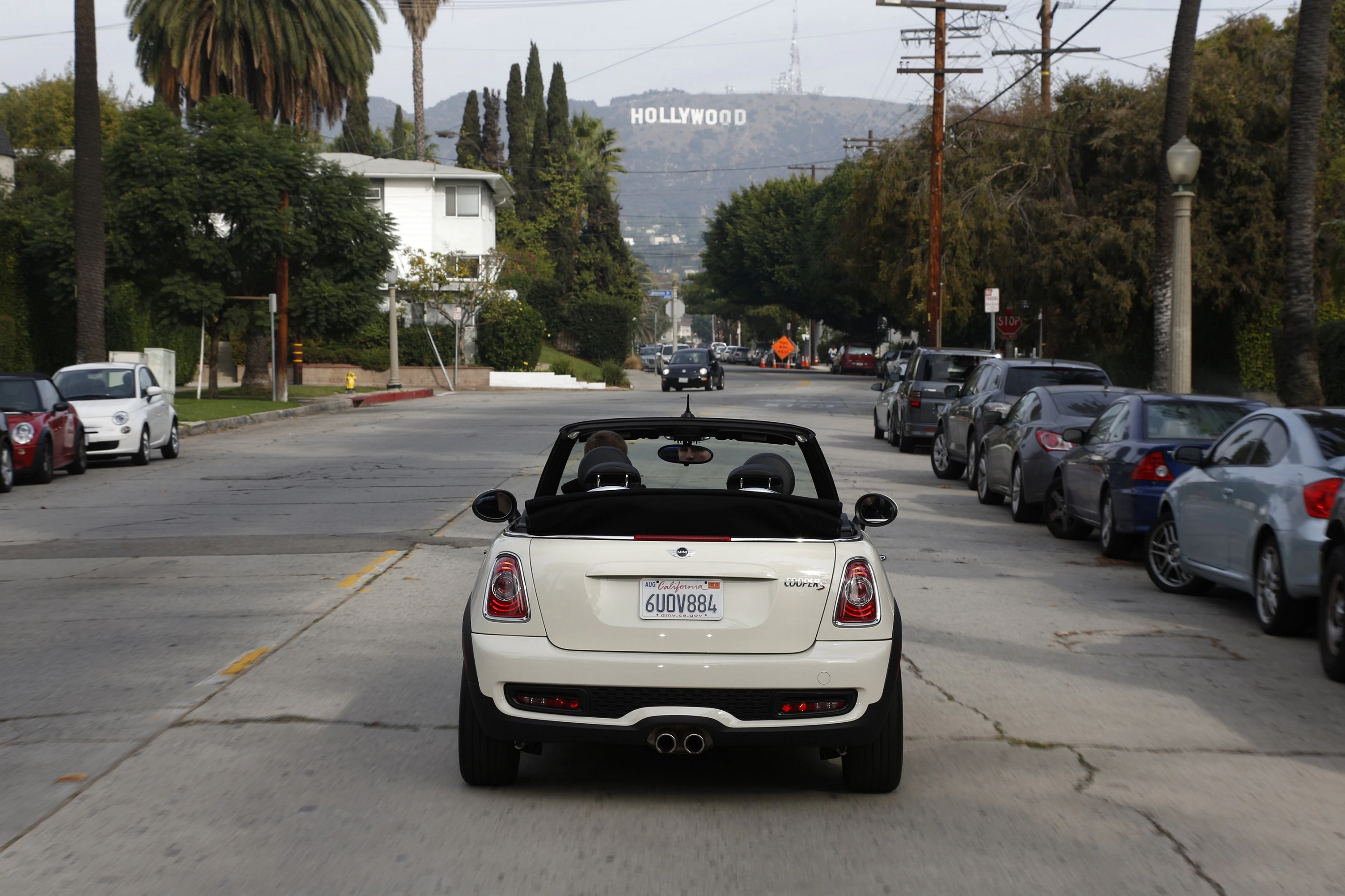 Ein weißes Cabrio fährt auf einer von Palmen gesäumten Straße in Richtung Hollywood-Schild in Los Angeles.