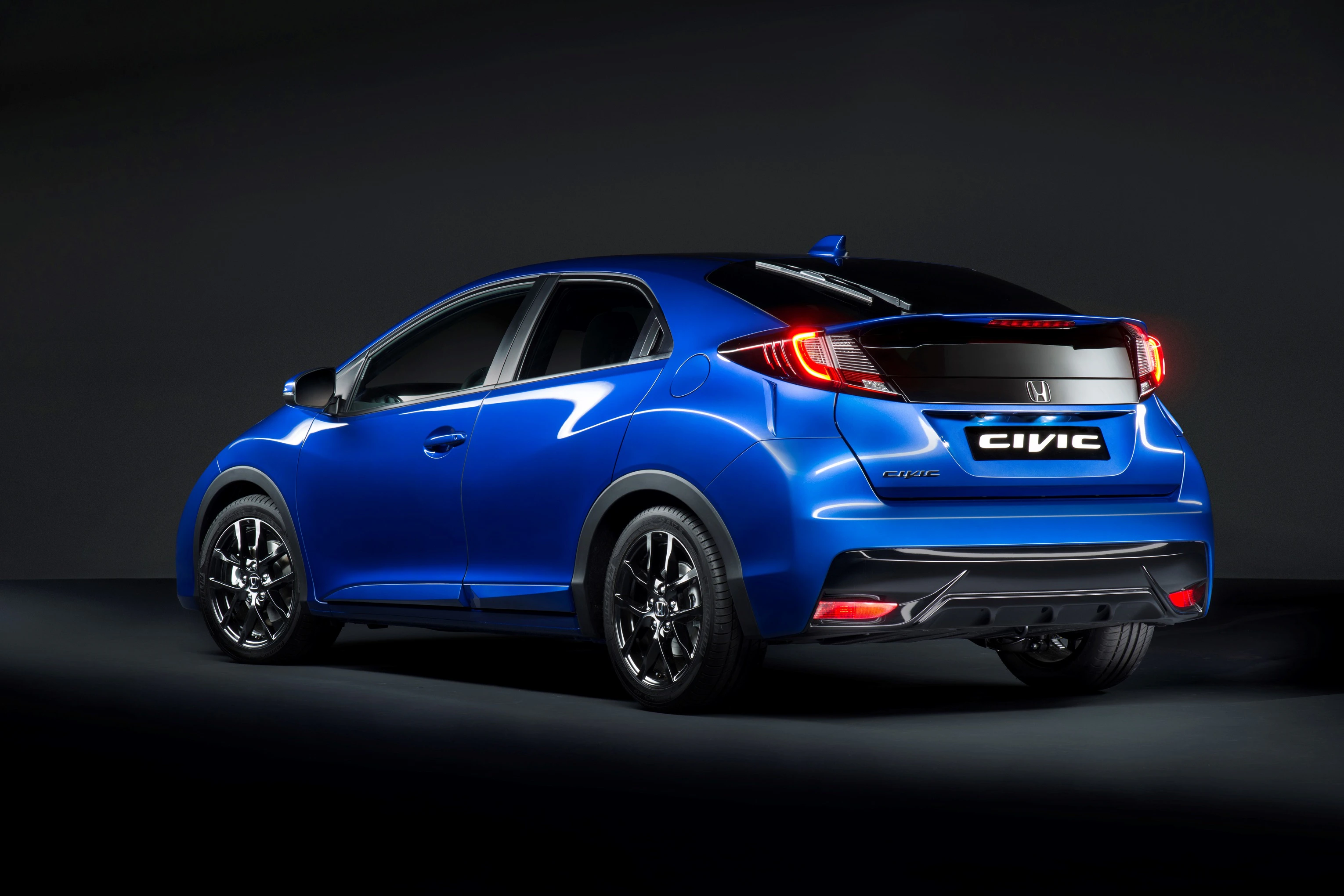 Blauer Honda Civic in Seitenansicht, auf dunklem Hintergrund. Das Auto hat sportliches Design mit auffällig glänzenden Felgen.