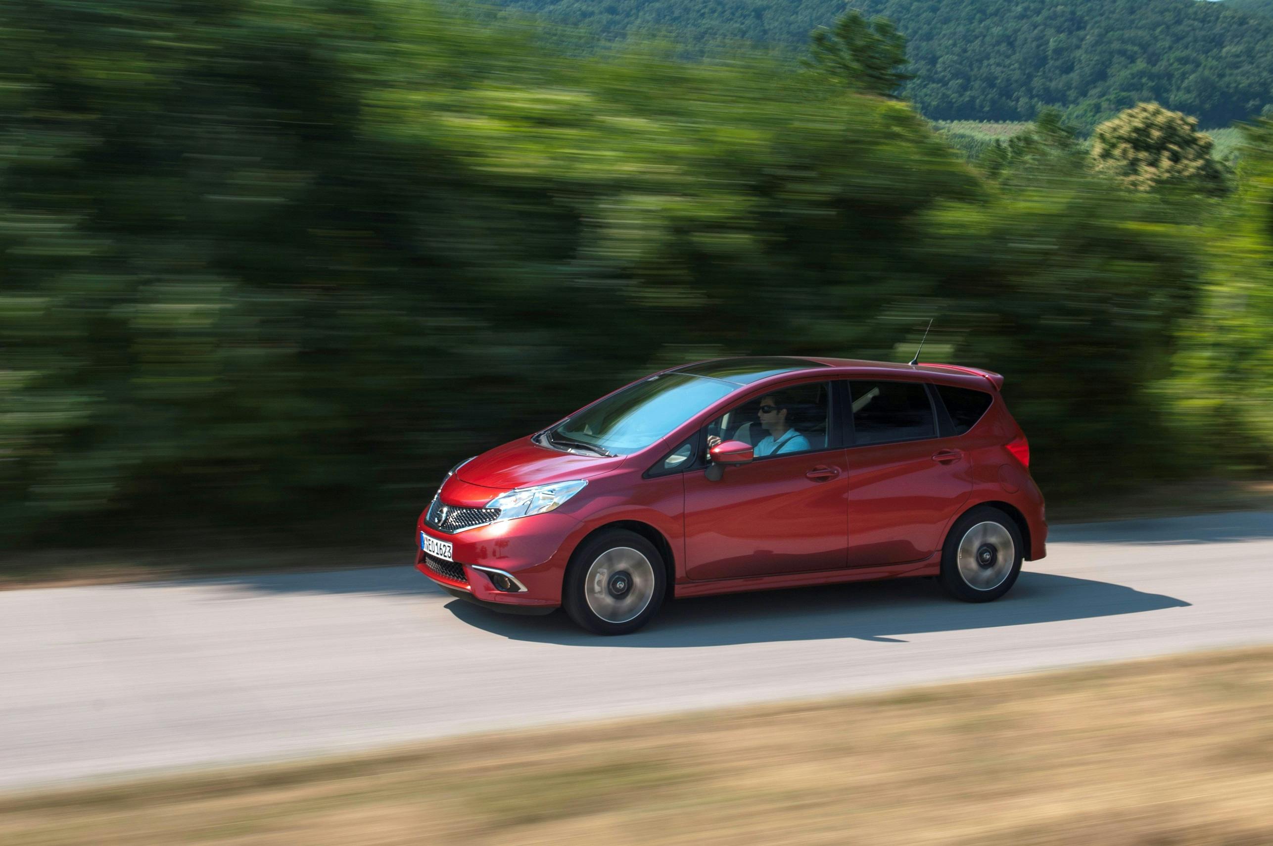Rotes Auto fährt schnell auf einer Landstraße, umgeben von verschwommenem grünen Laub im Hintergrund.