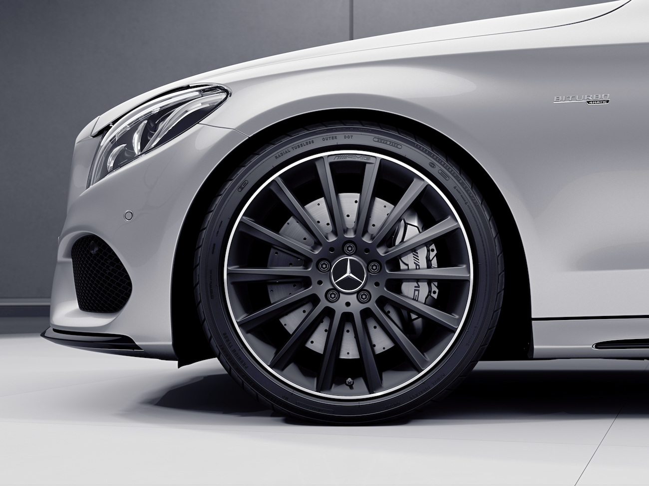 Nahaufnahme eines silbernen Mercedes-Benz mit AMG-Felge und Brembo-Bremse, sportliches Design, abgestellt in einem modernen Raum.