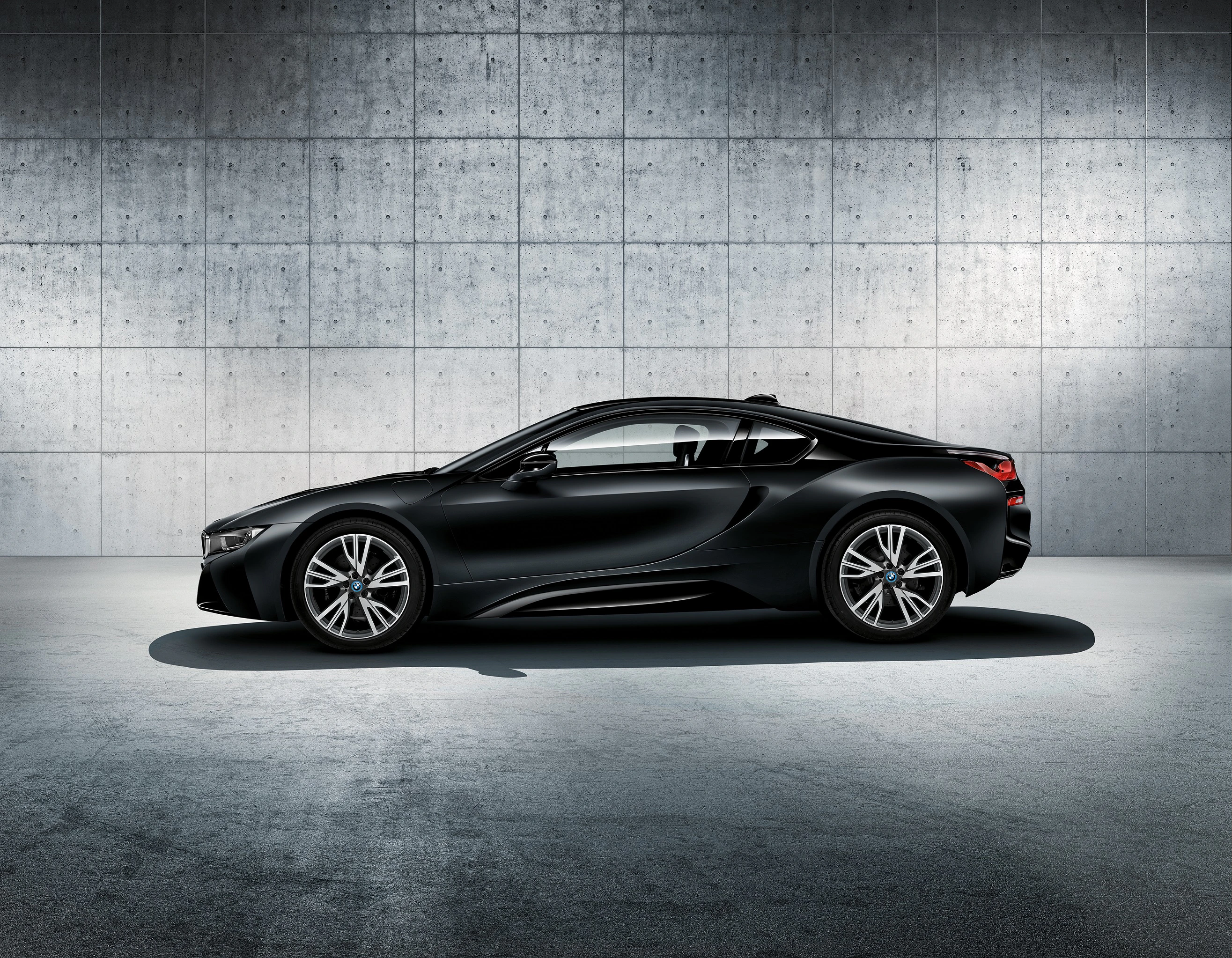 Schwarzes Sportcoupé steht seitlich in modernem, grauem Raum mit Betonwand. Elegante Linien, futuristisches Design.