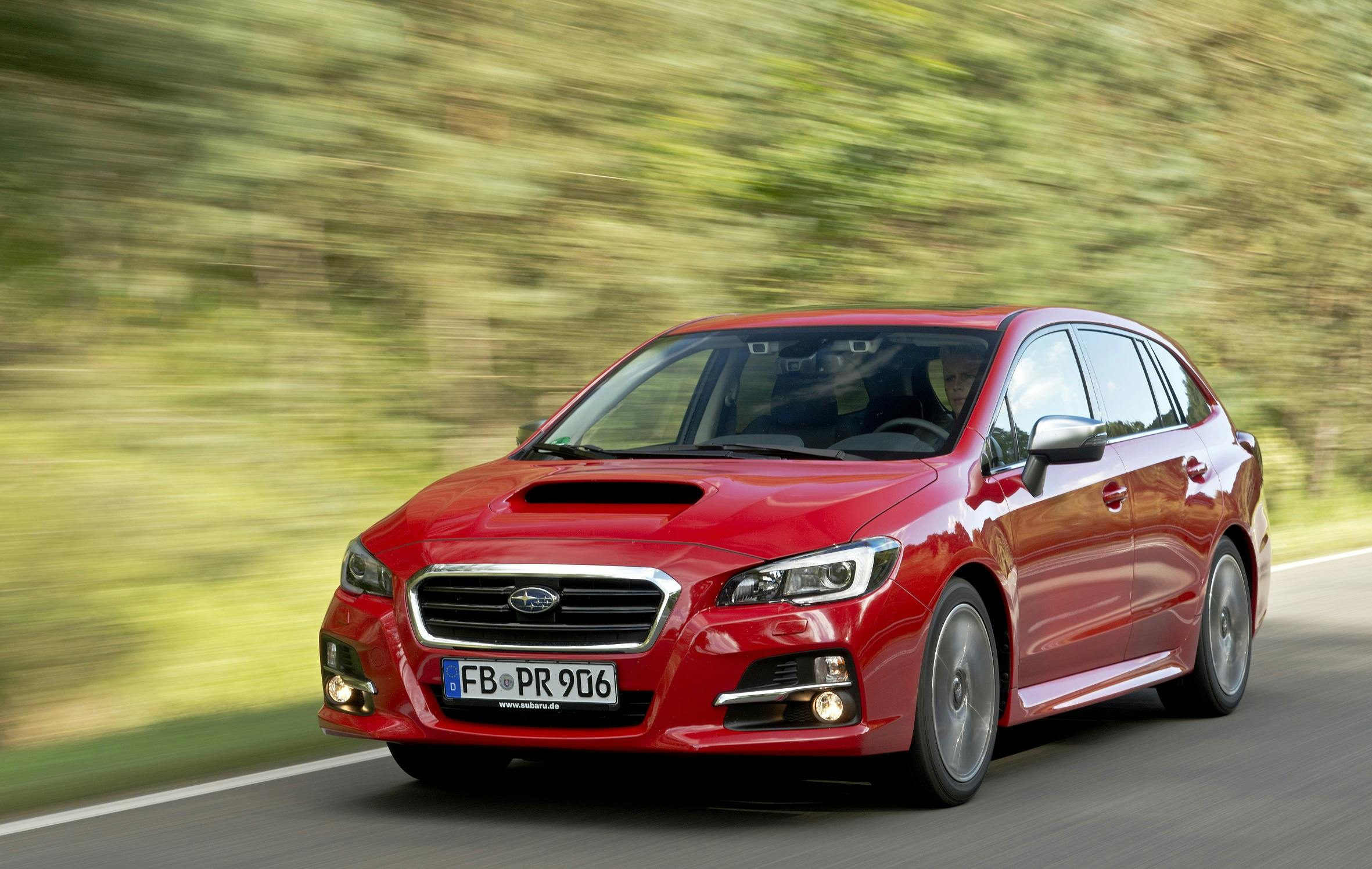 Roter Subaru Levorg fährt dynamisch auf einer Landstraße, umgeben von grüner, verschwommener Landschaft.