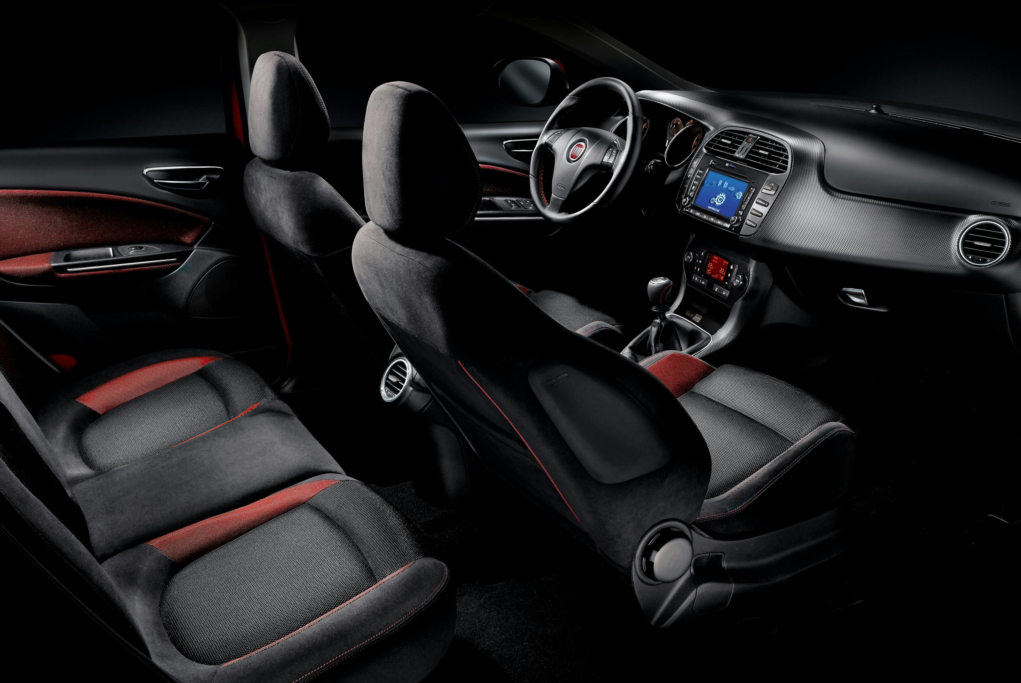 Innenraum eines modernen Autos mit dunklen Sitzen, roter Naht, Lenkrad, und digitalem Display auf dem Armaturenbrett.