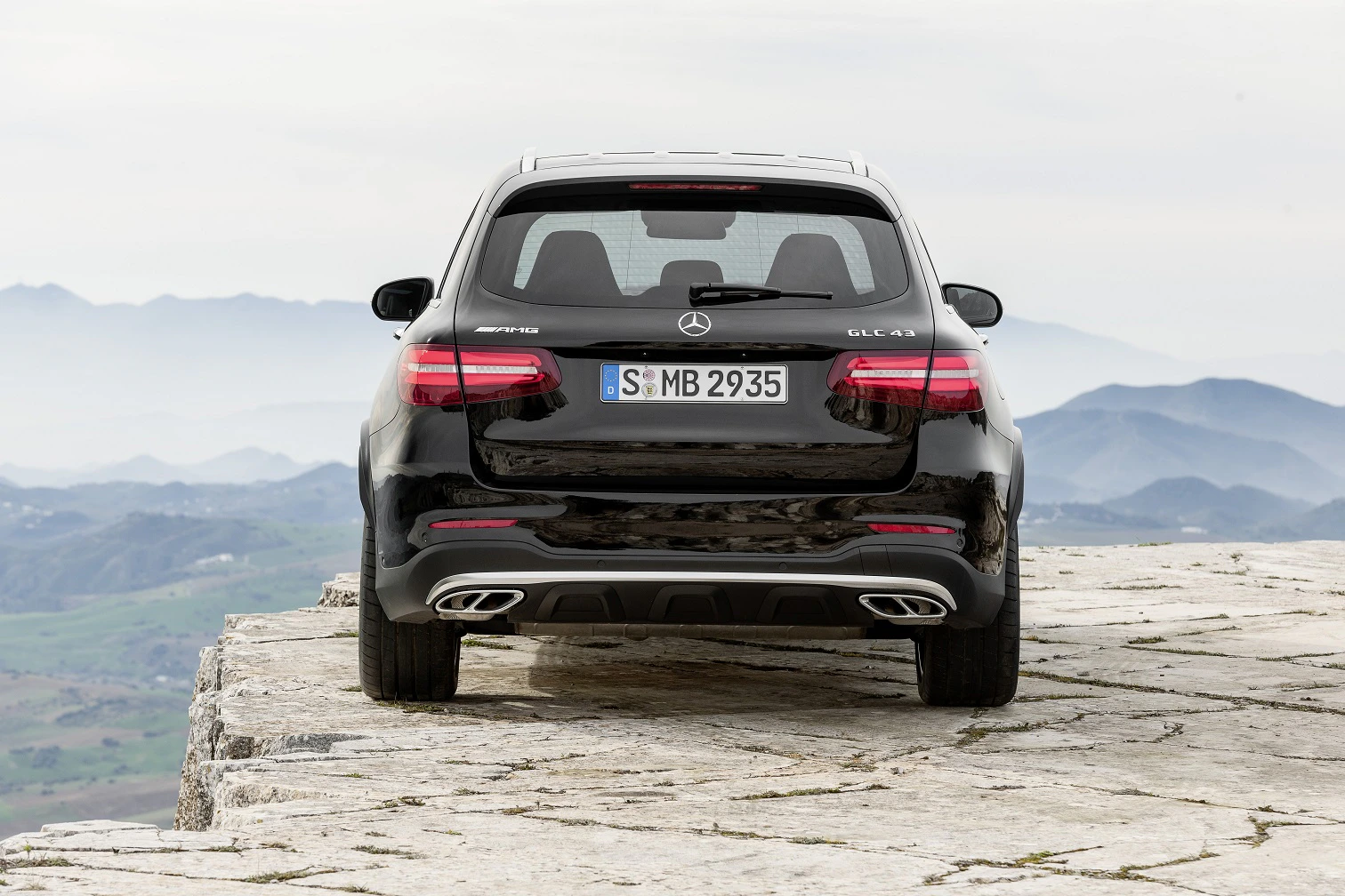 Schwarzer Mercedes-Benz SUV parkt auf einer steinigen Klippe, mit Blick auf eine weite, neblige Landschaft.