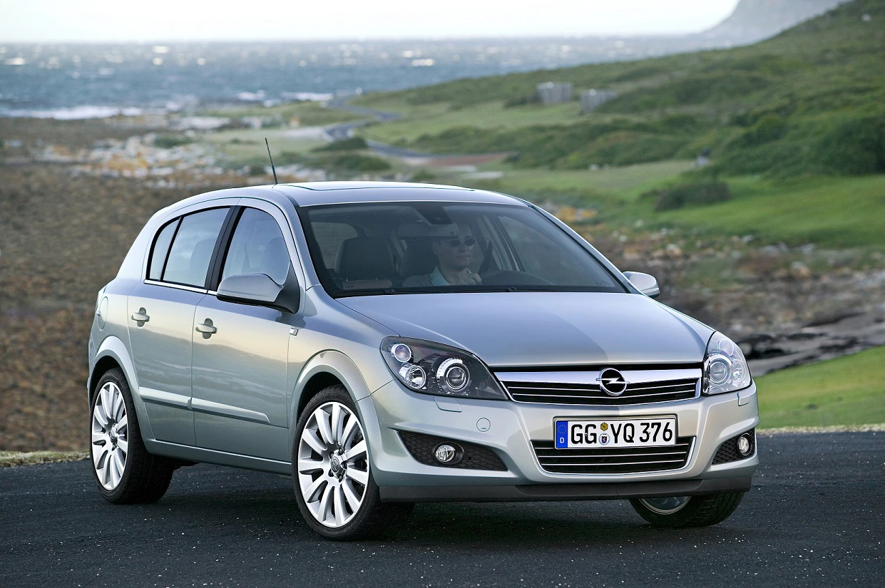 Silberner Opel Astra steht auf einer Straße vor einer grünen Landschaft und Meer im Hintergrund.