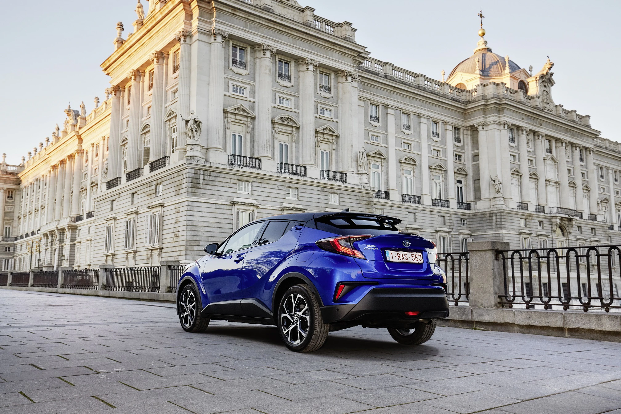 Blauer SUV parkt vor einem großen historischen Gebäude mit weißen Fassaden und reich verzierten Details, bei Sonnenuntergang.