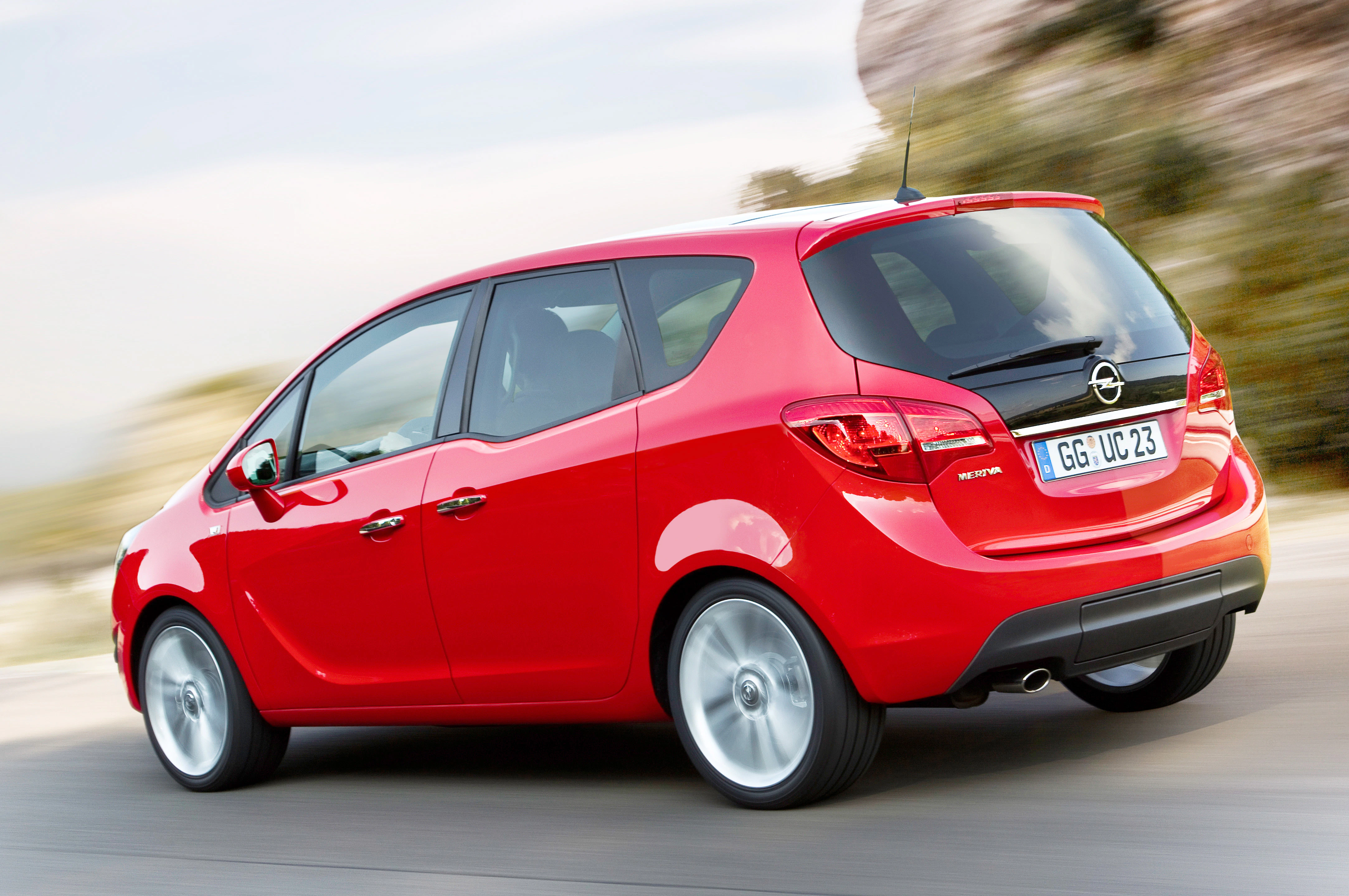 Roter Opel Zafira fährt auf einer Straße, von hinten betrachtet. Das Auto glänzt in der Sonne und die Umgebung ist leicht verschwommen.