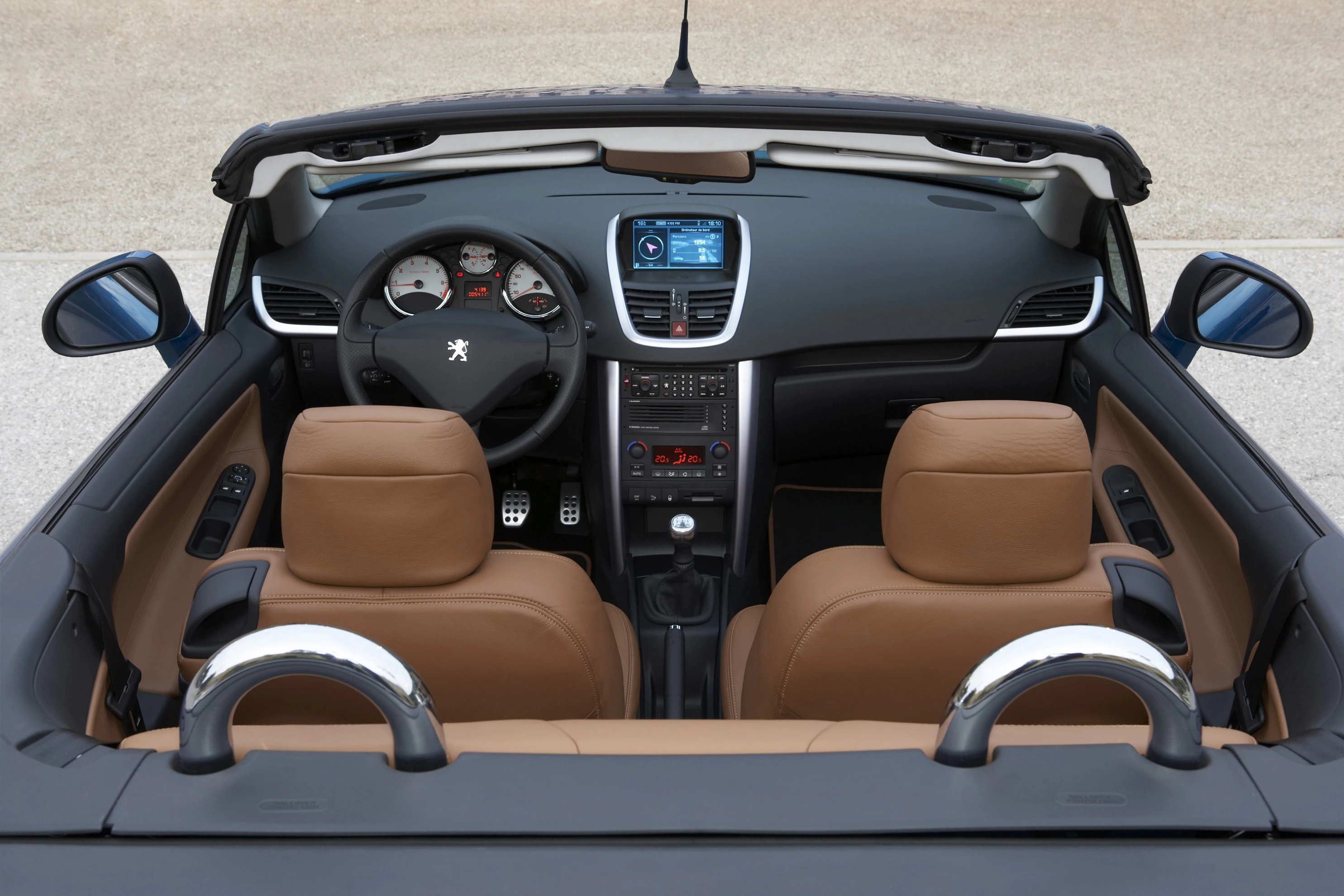 Innenansicht eines Peugeot-Cabrios mit braunen Ledersitzen, Lenkrad, Armaturenbrett mit Display und offenes Verdeck.