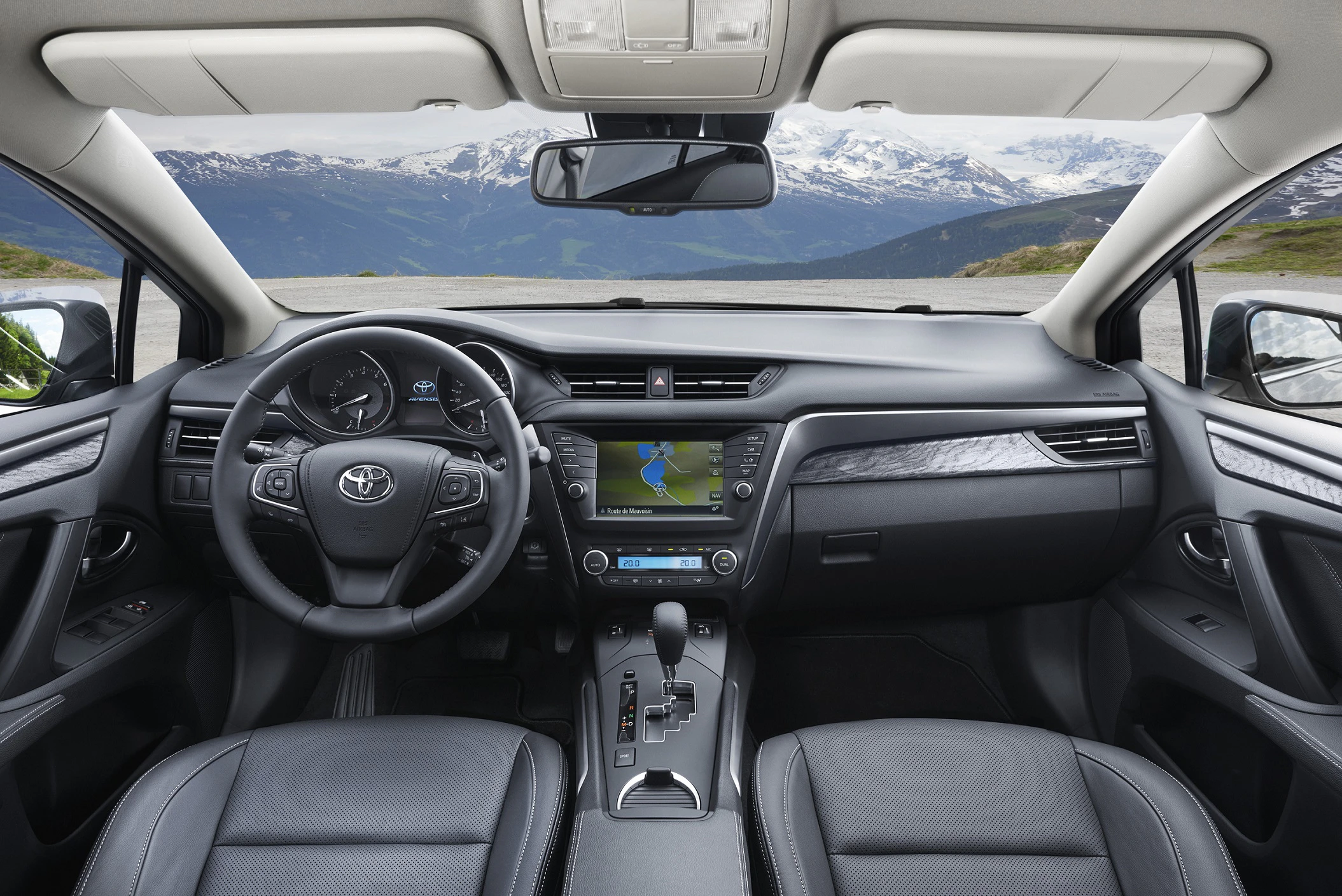 Innenraum eines Autos mit modernem Armaturenbrett und Navigationssystem. Blick auf eine verschneite Berglandschaft durch die Frontscheibe.