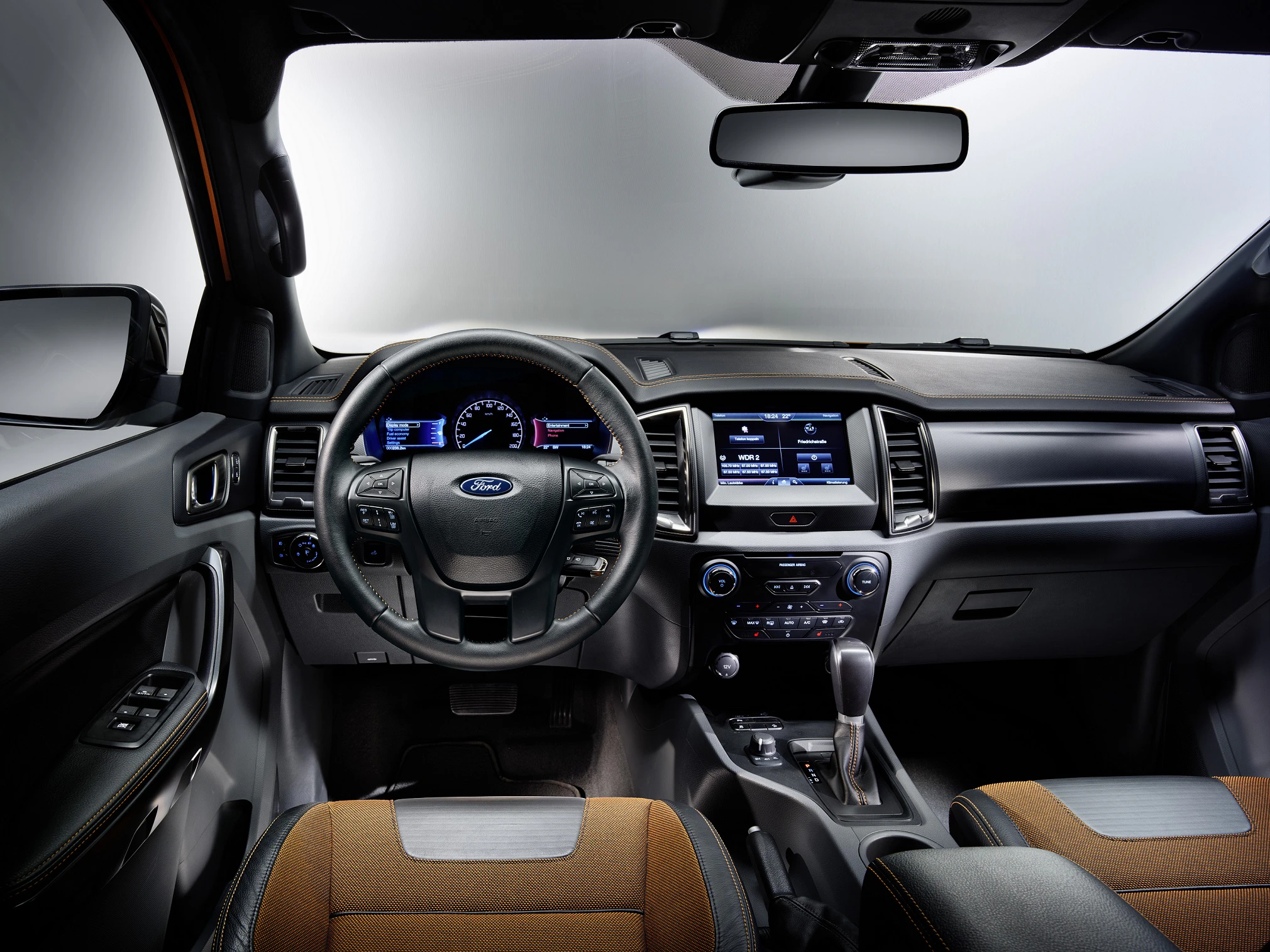 Innenraum eines Autos: Schwarzes Armaturenbrett mit braunen Ledersitzen. Multifunktionslenkrad, Touchscreen-Display und moderne Bedienelemente.