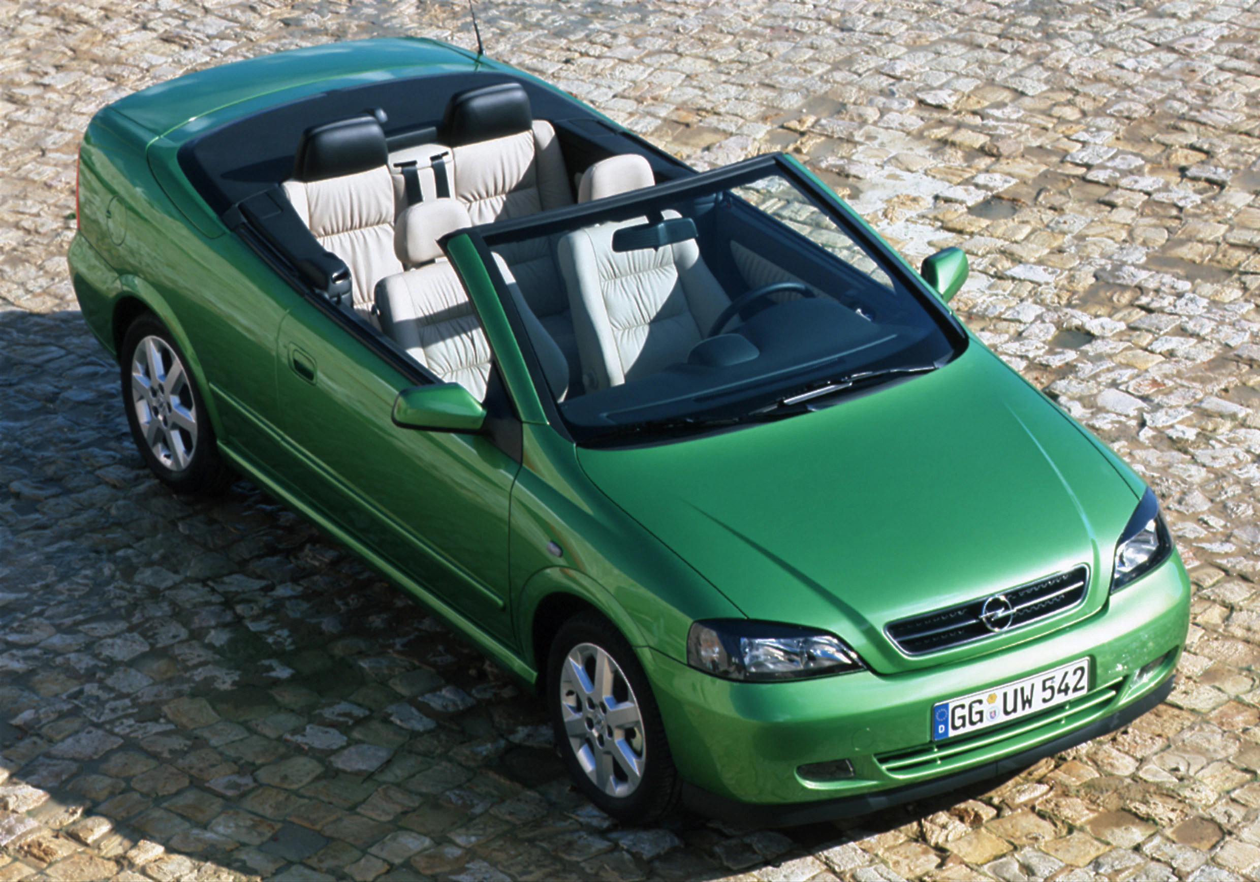 Grünes Cabriolet geparkt auf Kopfsteinpflaster. Das Auto hat ein offenes Verdeck und helle Ledersitze. Fahrzeugkennzeichen sichtbar.