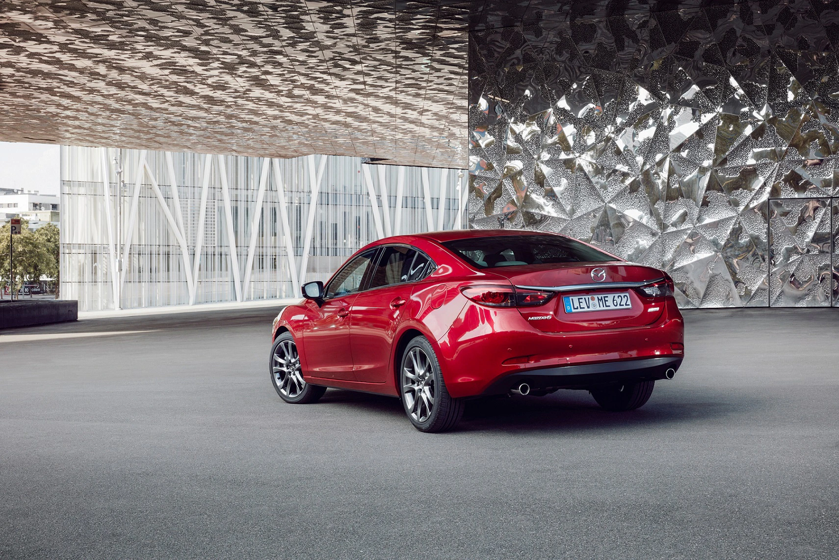 Roter Sportwagen geparkt vor einer modernen Fassade mit Glas und Metall. Lizenzschild sichtbar, Umgebung urban und futuristisch.