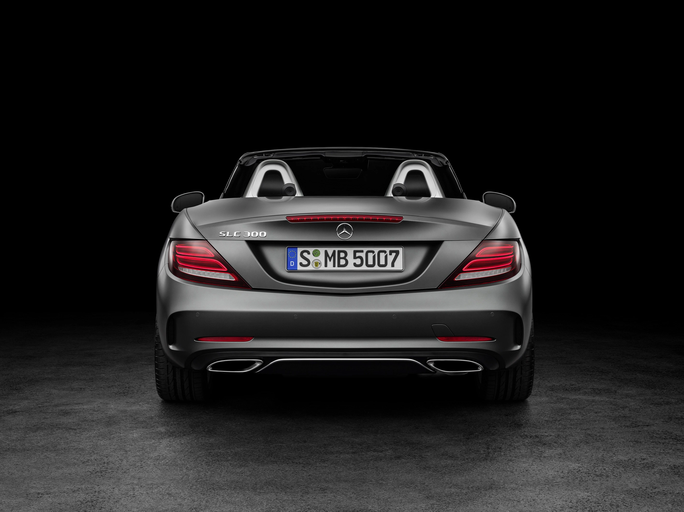 Rückansicht eines silbernen Mercedes-Benz SLC 300 Cabrios, mit hochgeklapptem Verdeck, auf dunklem Hintergrund.