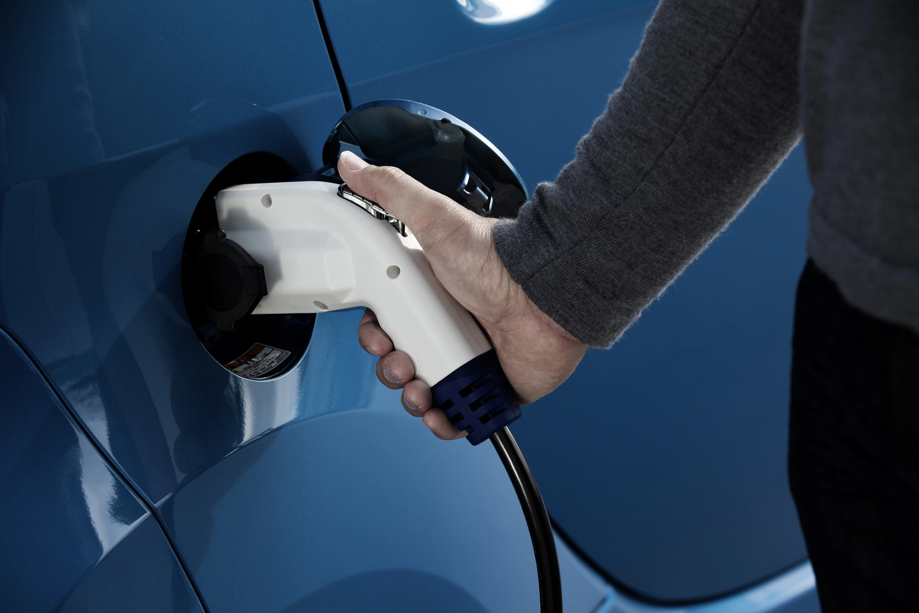 Hand steckt Ladekabel in ein blaues Elektroauto ein.