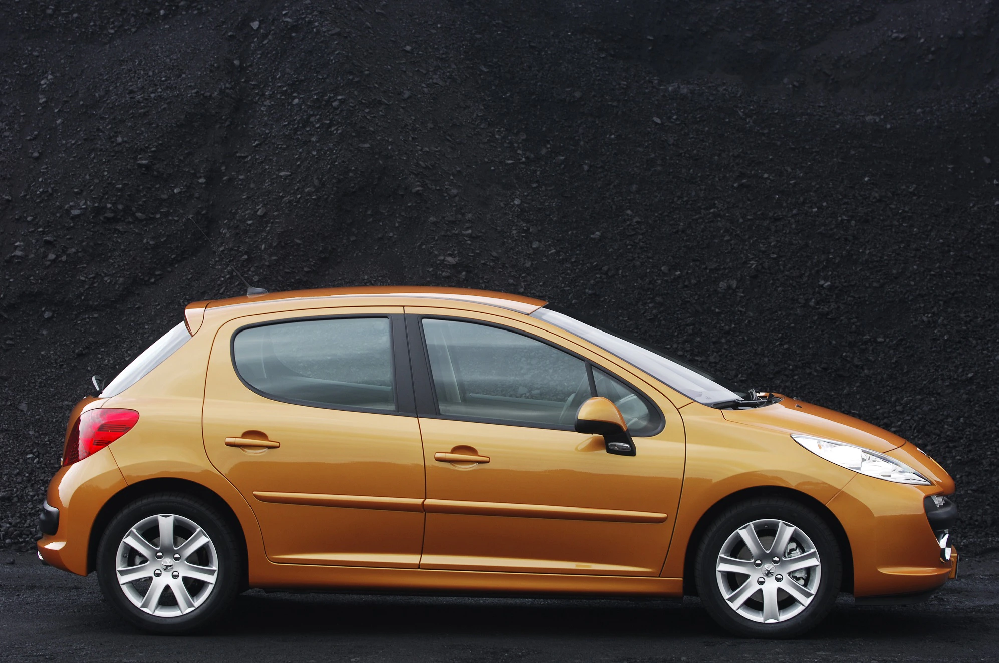 Orangefarbenes Auto der Kompaktklasse vor einem schwarzen Hintergrund, seitliche Ansicht.