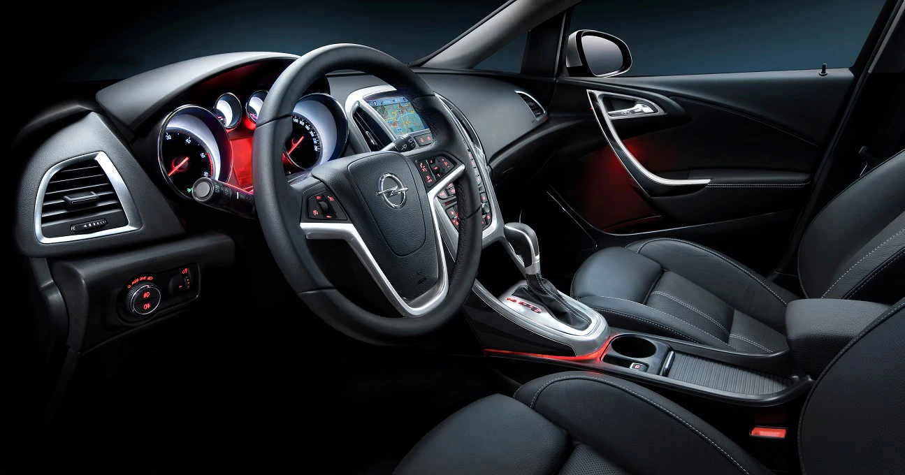 Innenraum eines modernen Autos mit Ledersitzen, beleuchtetem Armaturenbrett, Lenkrad und Mittelkonsole mit roten Akzenten.