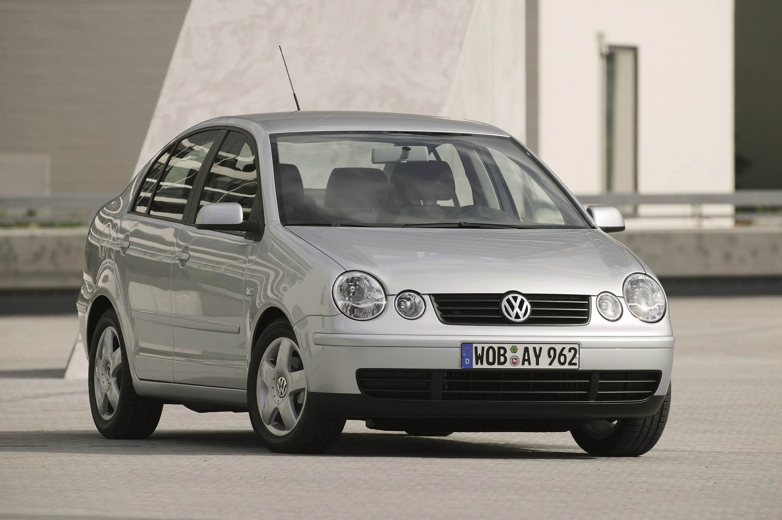 Silberner Volkswagen Polo, Frontansicht. Fahrzeug steht auf einer gepflasterten Fläche vor einem modernen Gebäude.