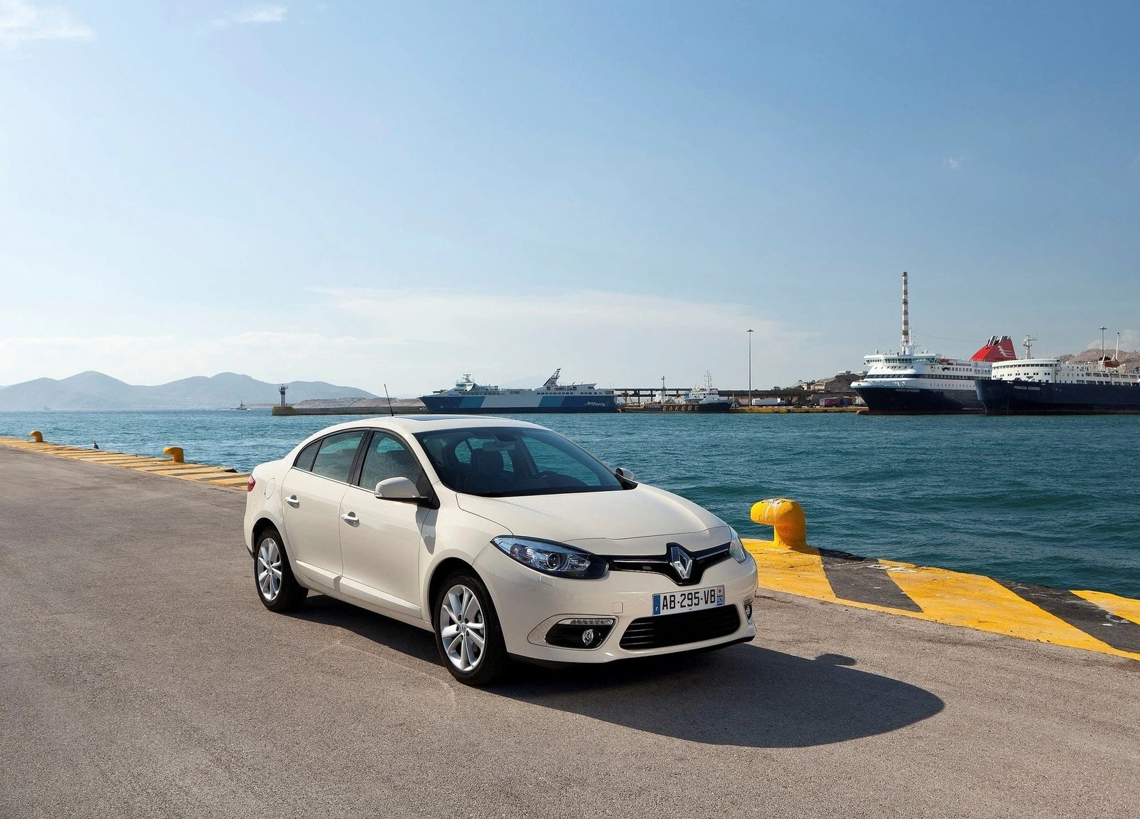 Ein weißer Renault auf einem Hafengelände mit Schiffen im Hintergrund und blauem Himmel. Schreiblinien markieren den Kai.