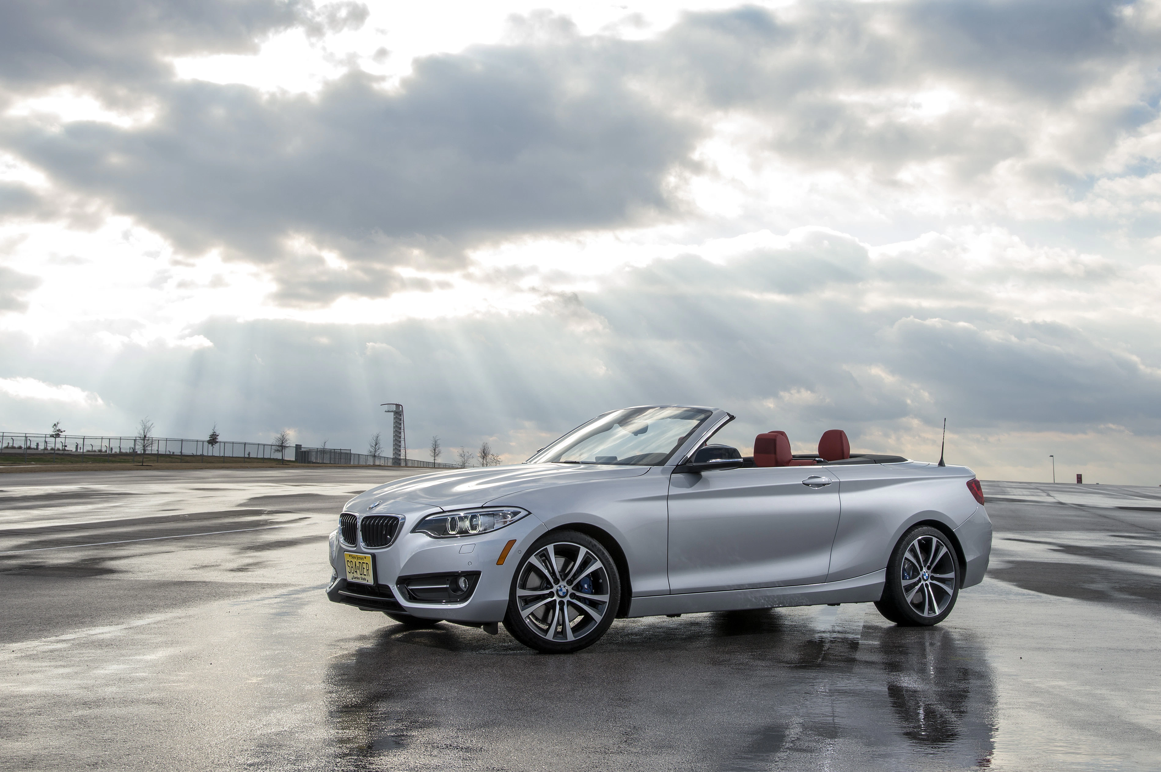 Silbernes Cabriolet auf nasser Straße, Sonnenstrahlen durch Wolken.