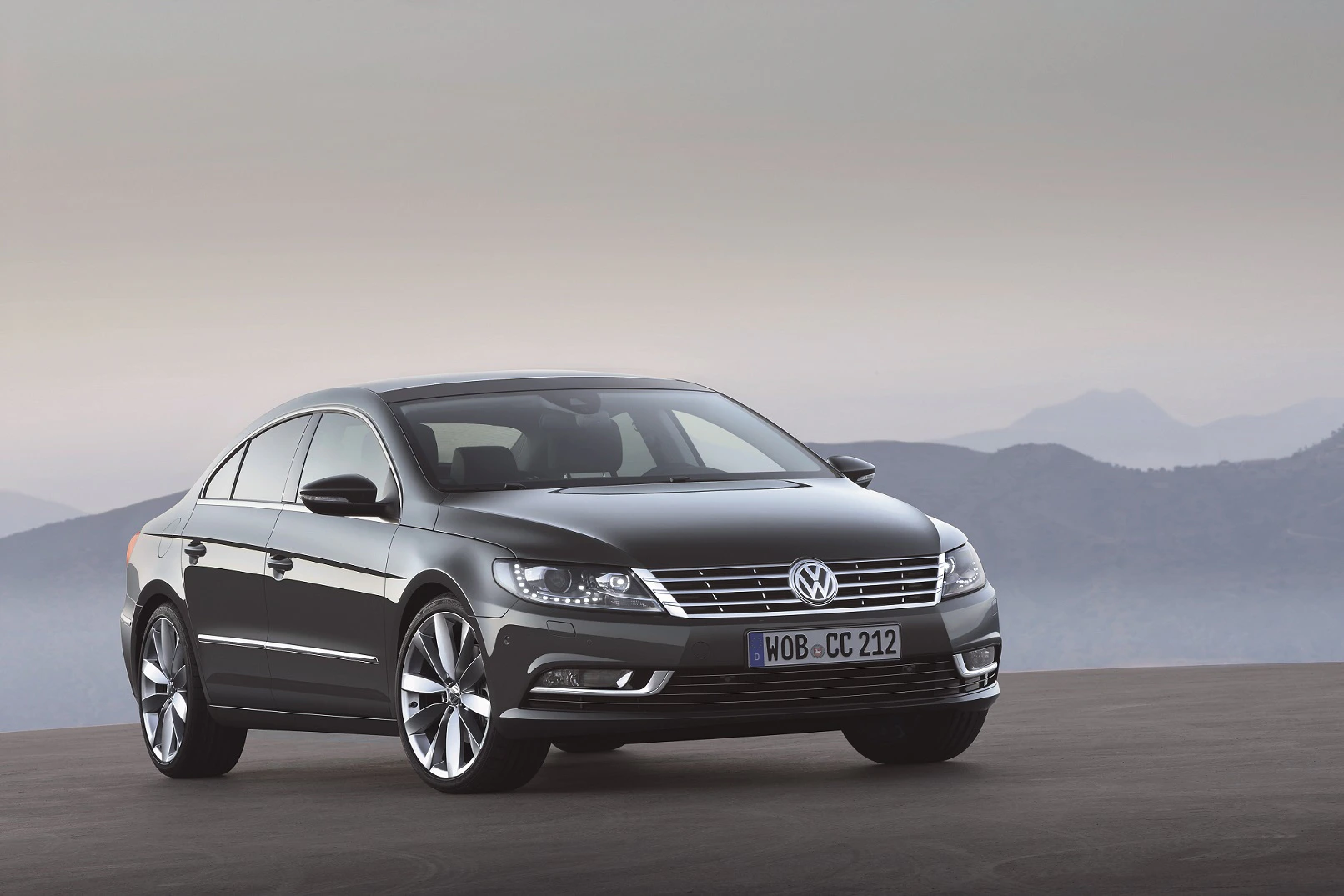 Schwarzer VW Passat CC auf einem Berg mit nebliger Landschaft im Hintergrund. Elegantes Design, seitlich von vorne fotografiert.