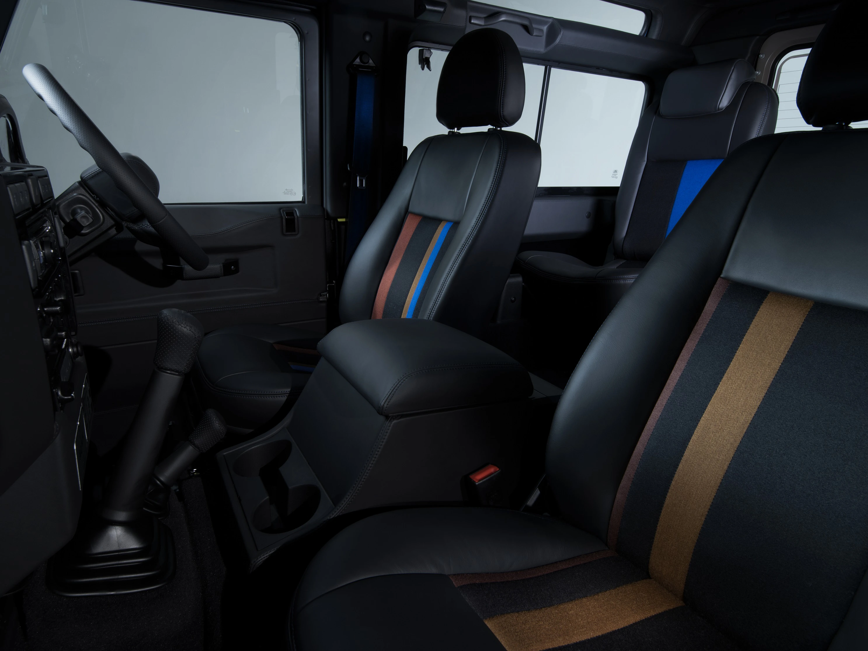 Innenraum eines Autos mit schwarzen Ledersitzen, mehrfarbigen Streifen akzentuiert. Dunkle Armaturen und Lenkrad sind sichtbar.
