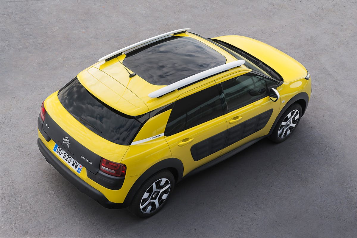 Gelber Citroën C4 Cactus mit schwarzen Airbumps und Panorama-Glasdach, von oben fotografiert auf grauem Asphaltboden.