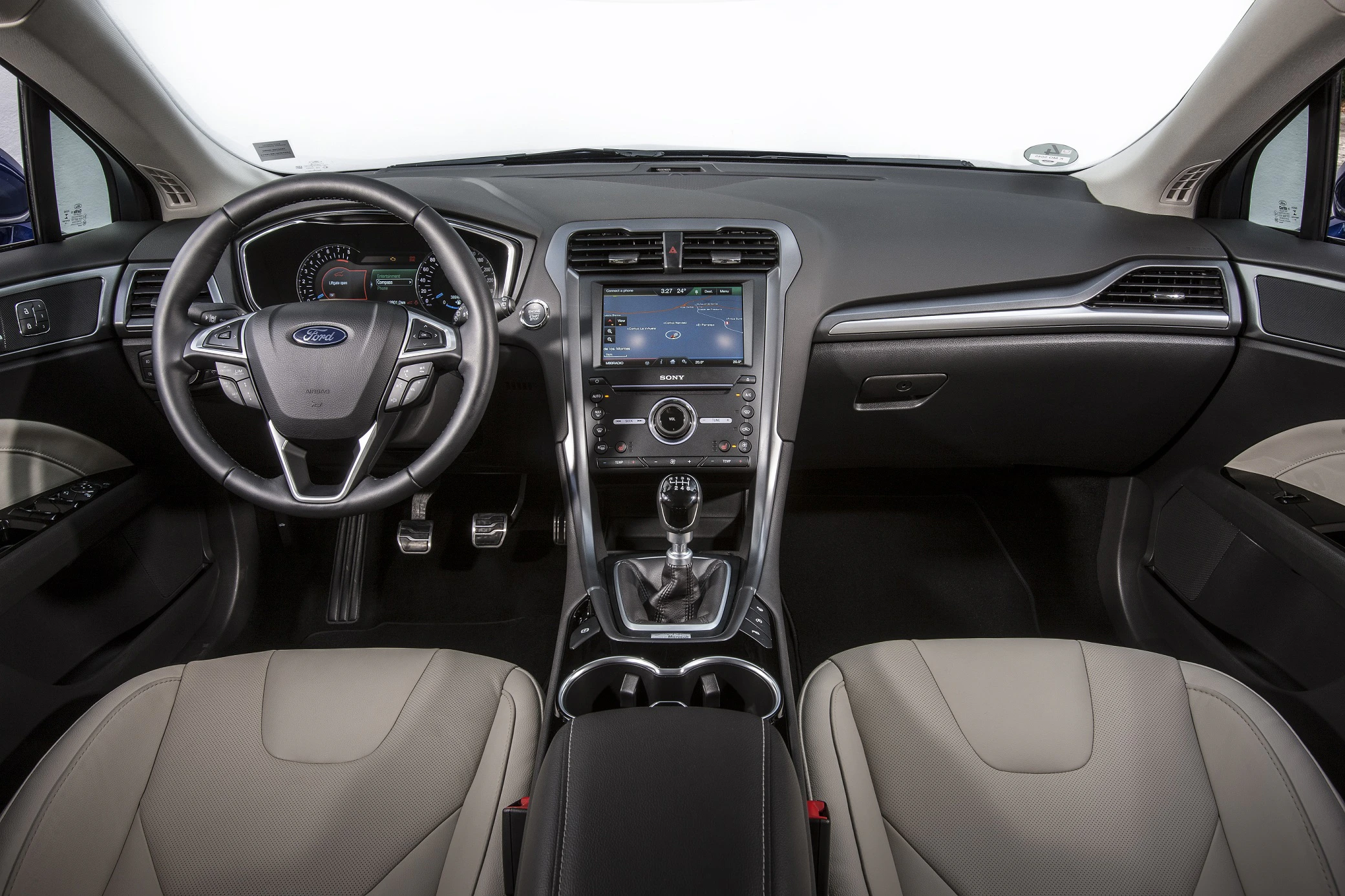 Innenansicht eines Autos mit modernem Armaturenbrett, Lenkrad, Schalthebel und Touchscreen-Mittelkonsole. Beige und schwarze Sitze.