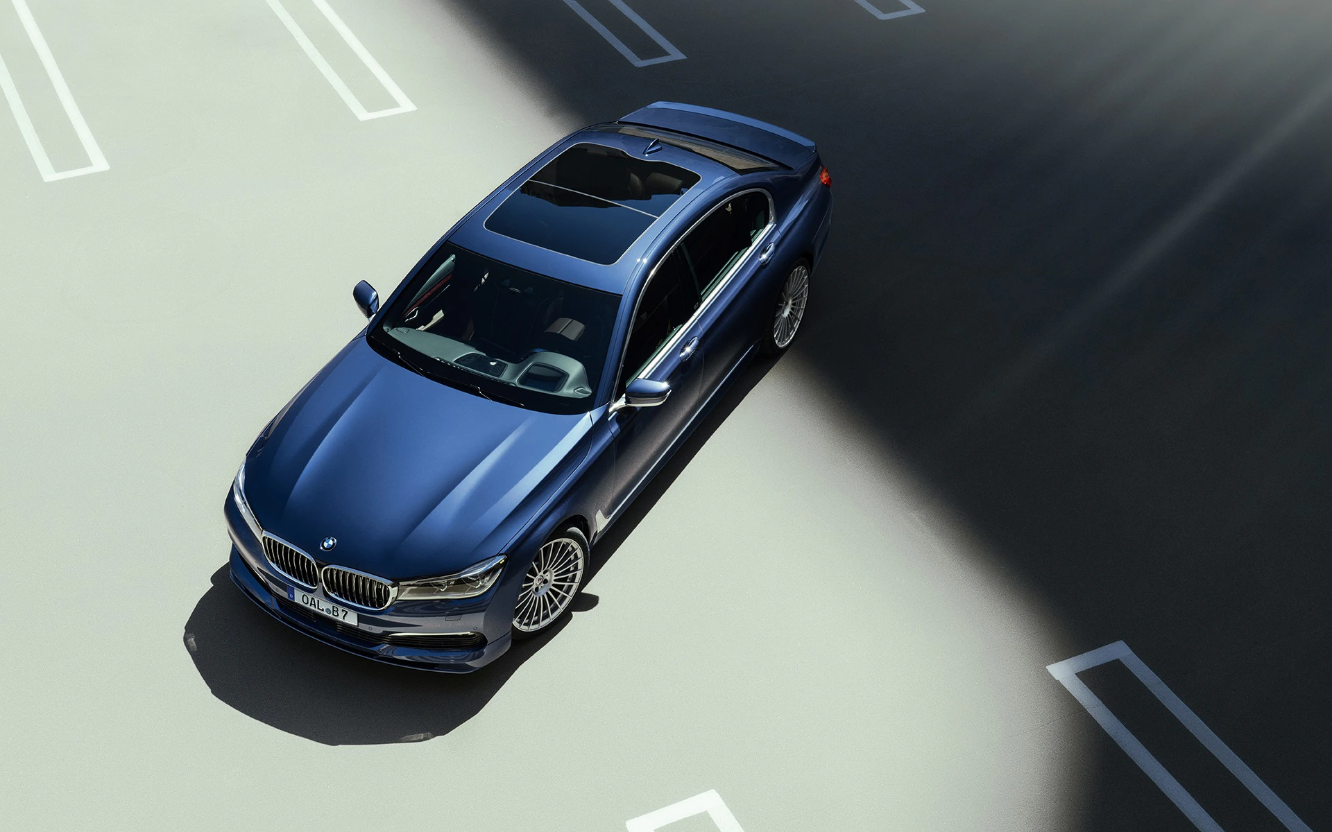 Blauer BMW auf einem Parkplatz in einem Sonnenstrahl, fotografiert aus der Vogelperspektive.
