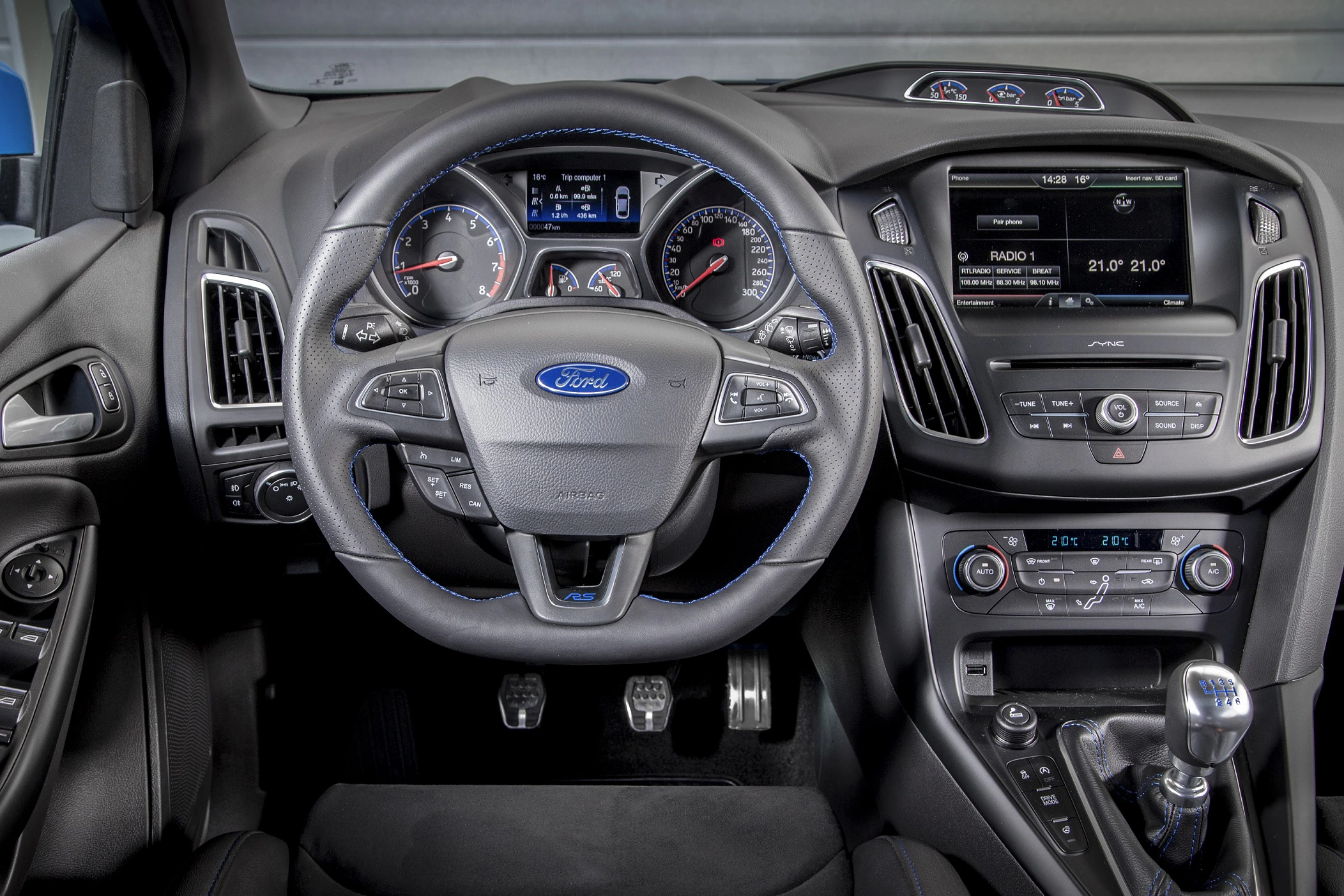 Innenraum eines Ford mit Lenkrad, Tachometer, Infotainmentsystem und Schalthebel. Moderne Ausstattung und Bedienelemente.
