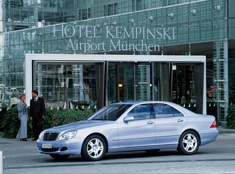 Silberner Mercedes-Benz vor dem Hotel Kempinski am Flughafen München, mit zwei Personen im Hintergrund.