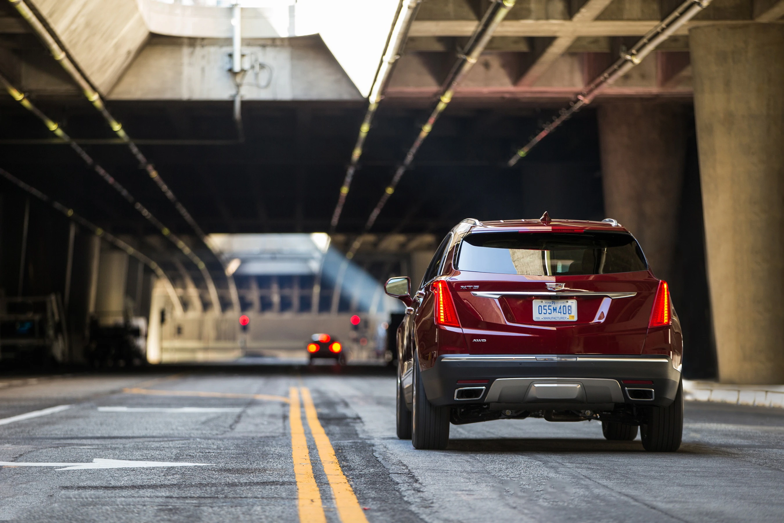 Roter SUV fährt durch einen Tunnel unter einer Brücke. Zwei Fahrzeuge vorne und moderne Architektur im Hintergrund. Tageslicht fällt ein.